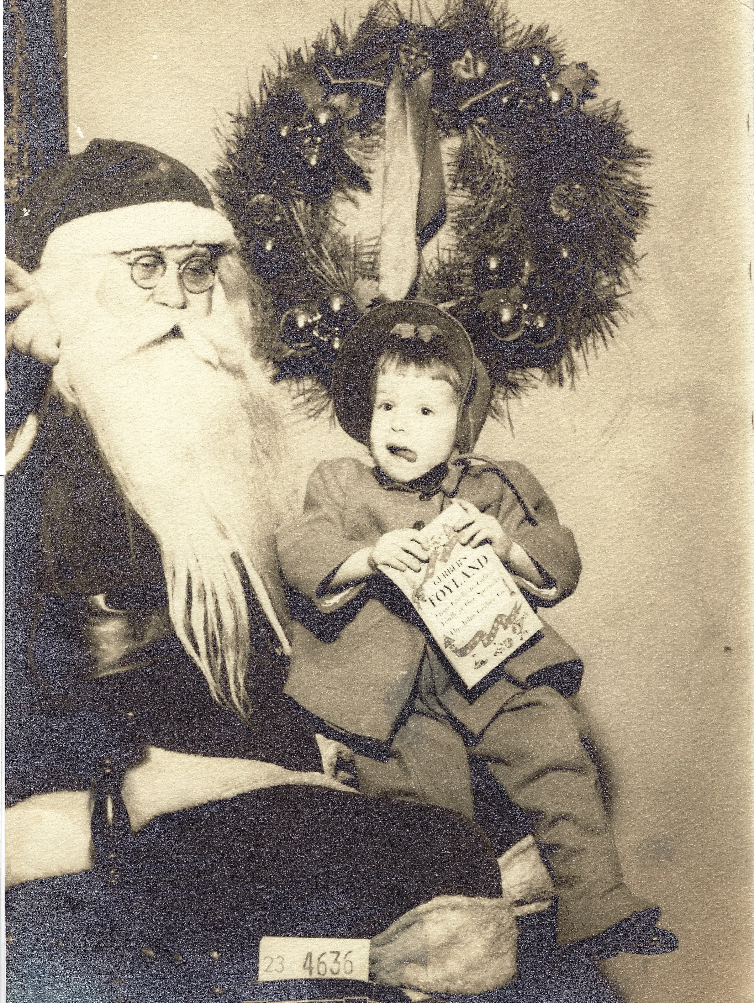 A young child sitting with Santa and holding a card, sepia studio print, around 1955, from Cacky's collection