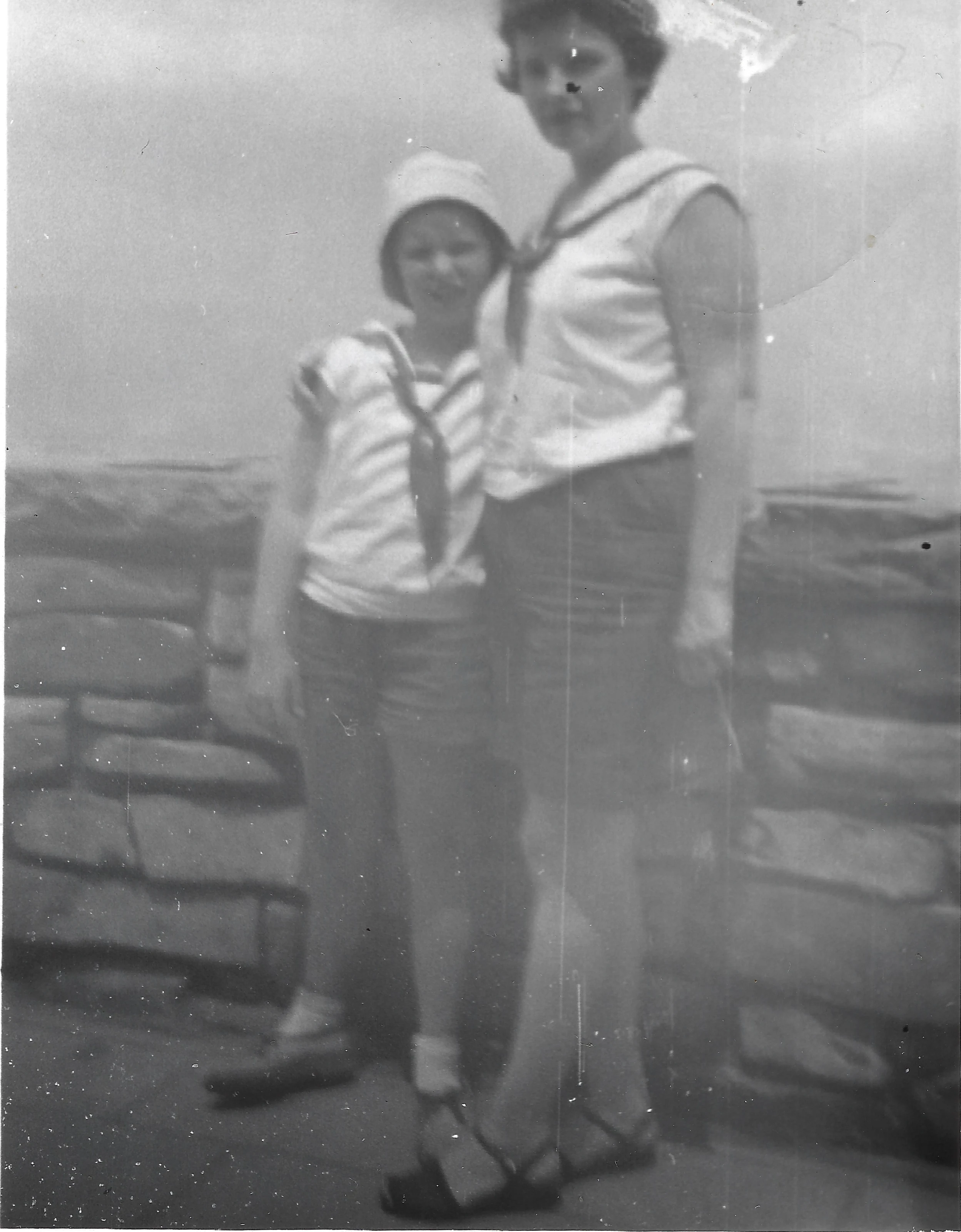 A child and a taller young woman in matching sailor tops posing by a low stone wall on a hazy day, around 1956, from Cacky's collection