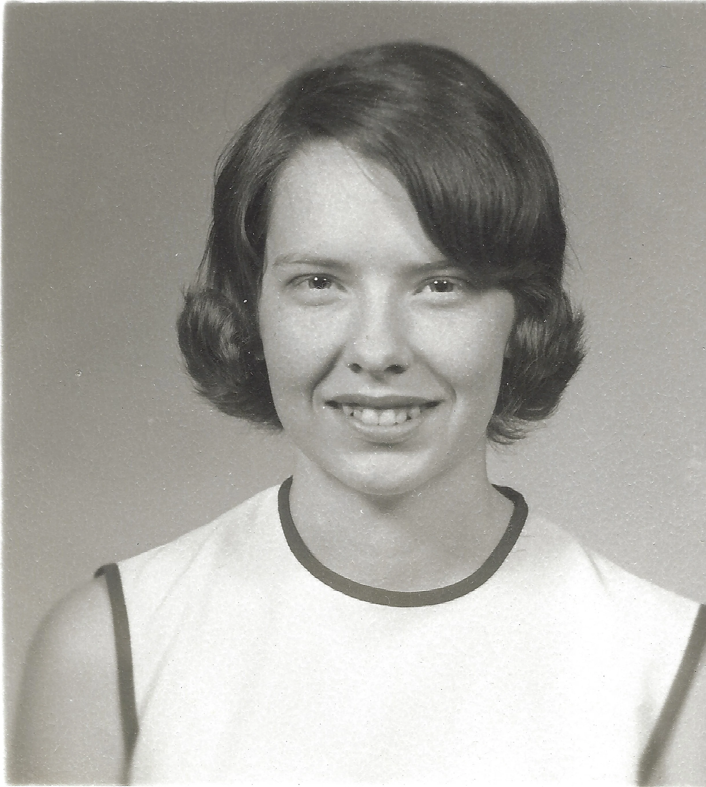 A black-and-white school portrait of Cacky as a young woman in a white sleeveless top with dark trim, around 1964