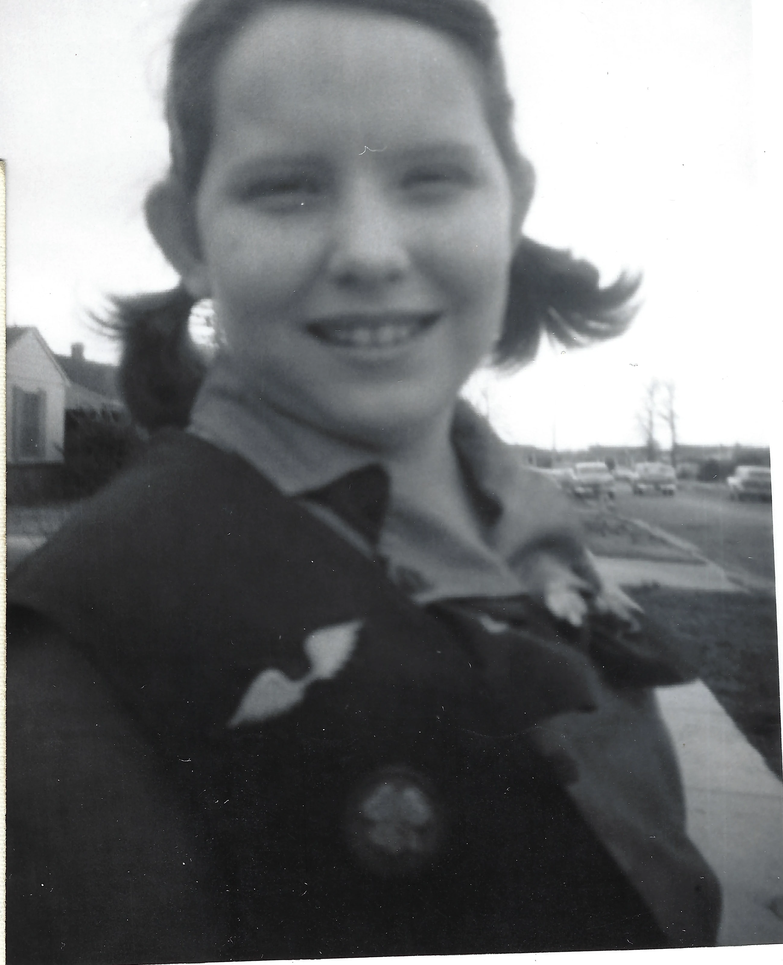 A candid close-up of Cacky in a Girl Scout uniform with pigtails, outdoors, around 1958