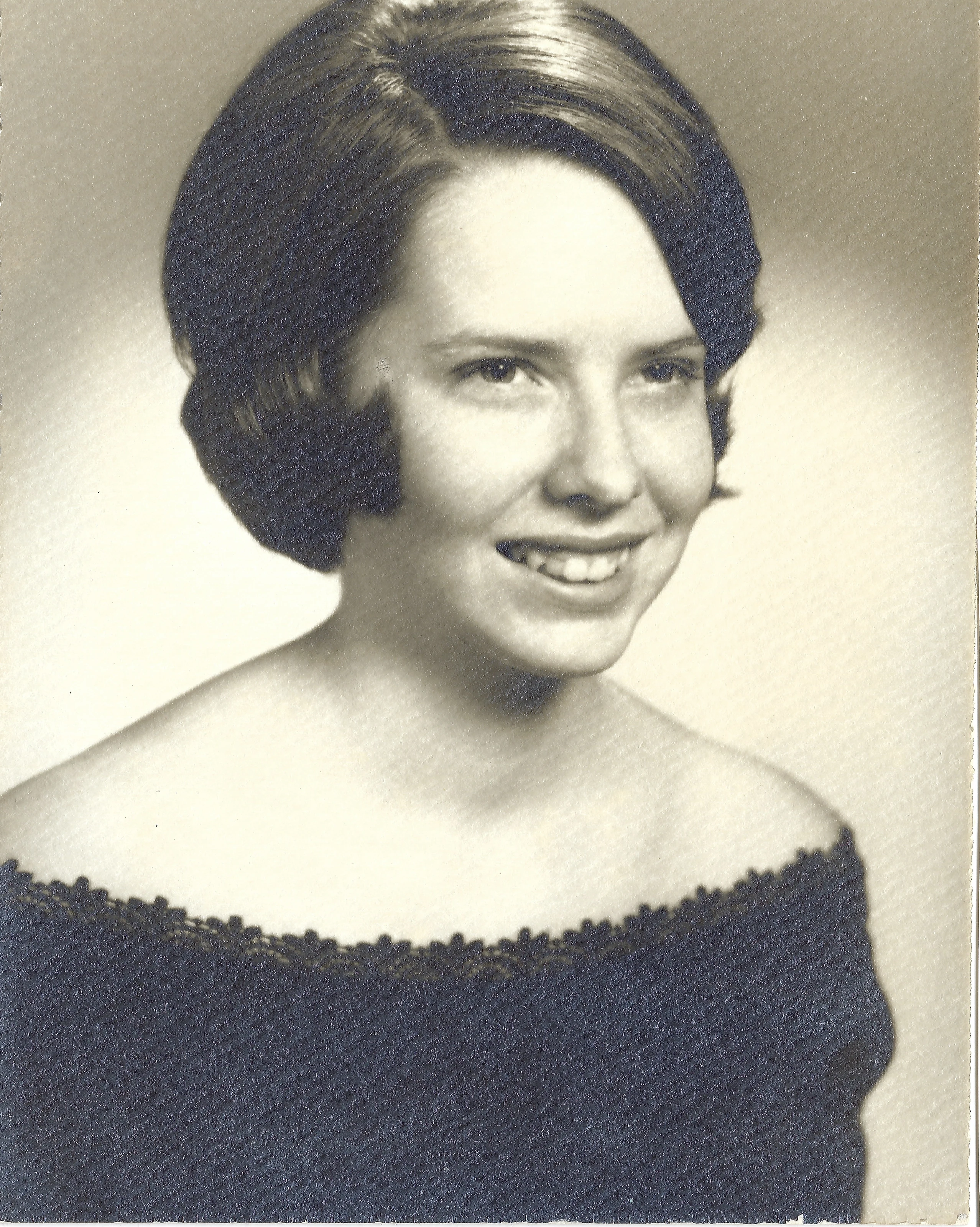 A formal studio portrait of Cacky as a young woman in an off-the-shoulder dark dress, around 1965