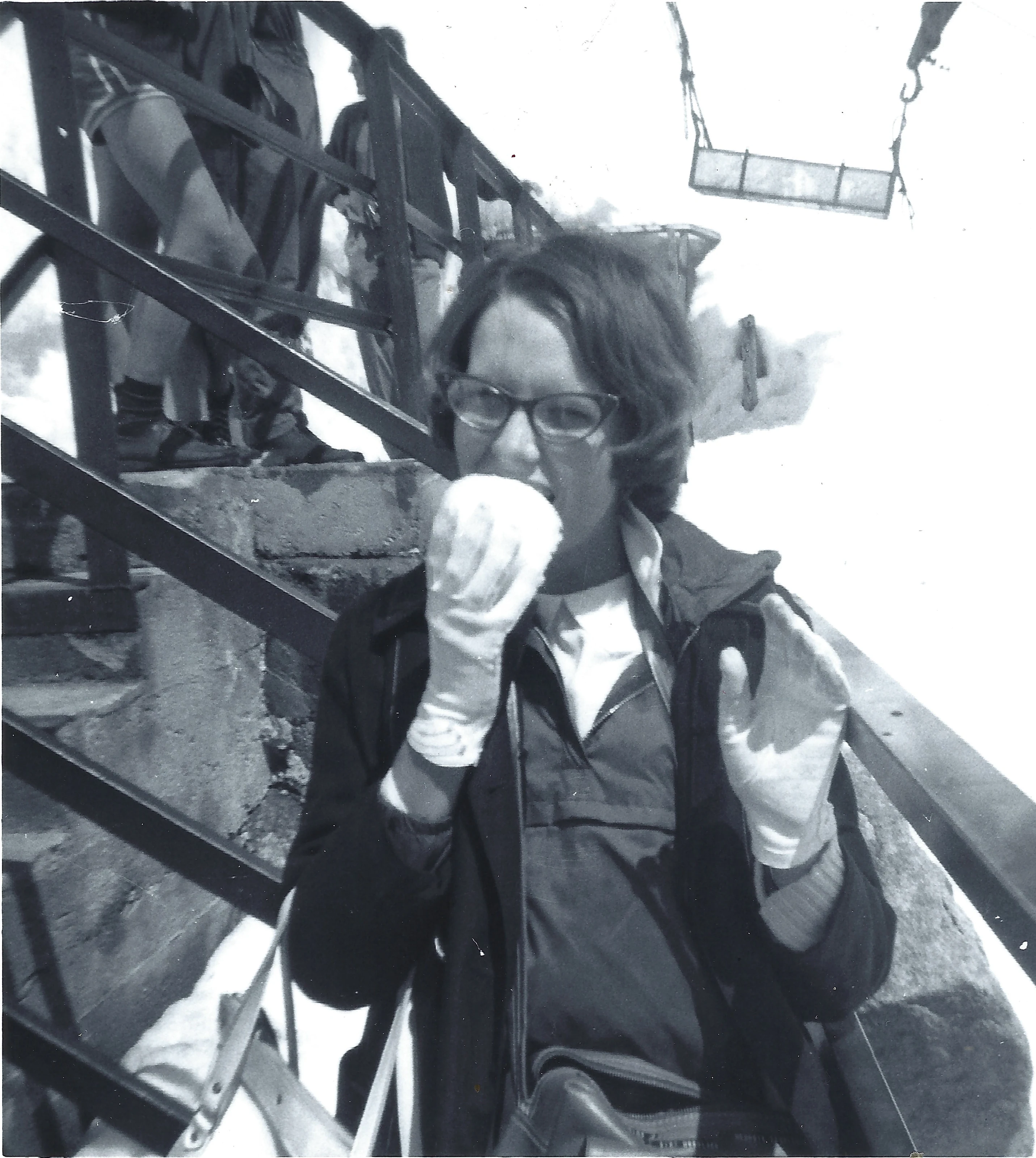 A young woman in glasses and white gloves striking a playful boxing pose on a metal observation-tower staircase, others behind, around 1966, from Cacky's collection