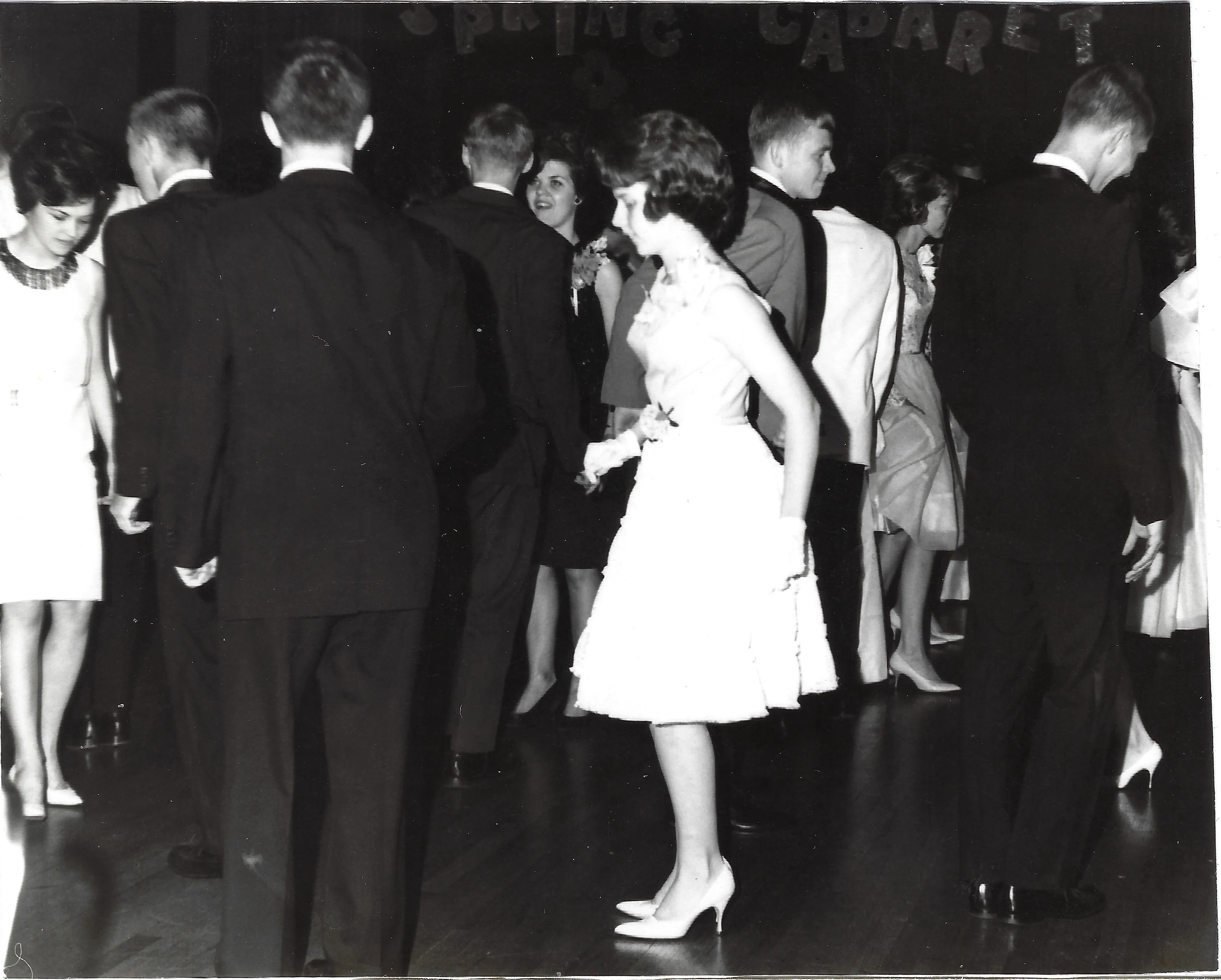 Cacky (b.1947) in a white ruffled dress and gloves on the floor at a 'Spring Cabaret' dance, couples around her, around 1966