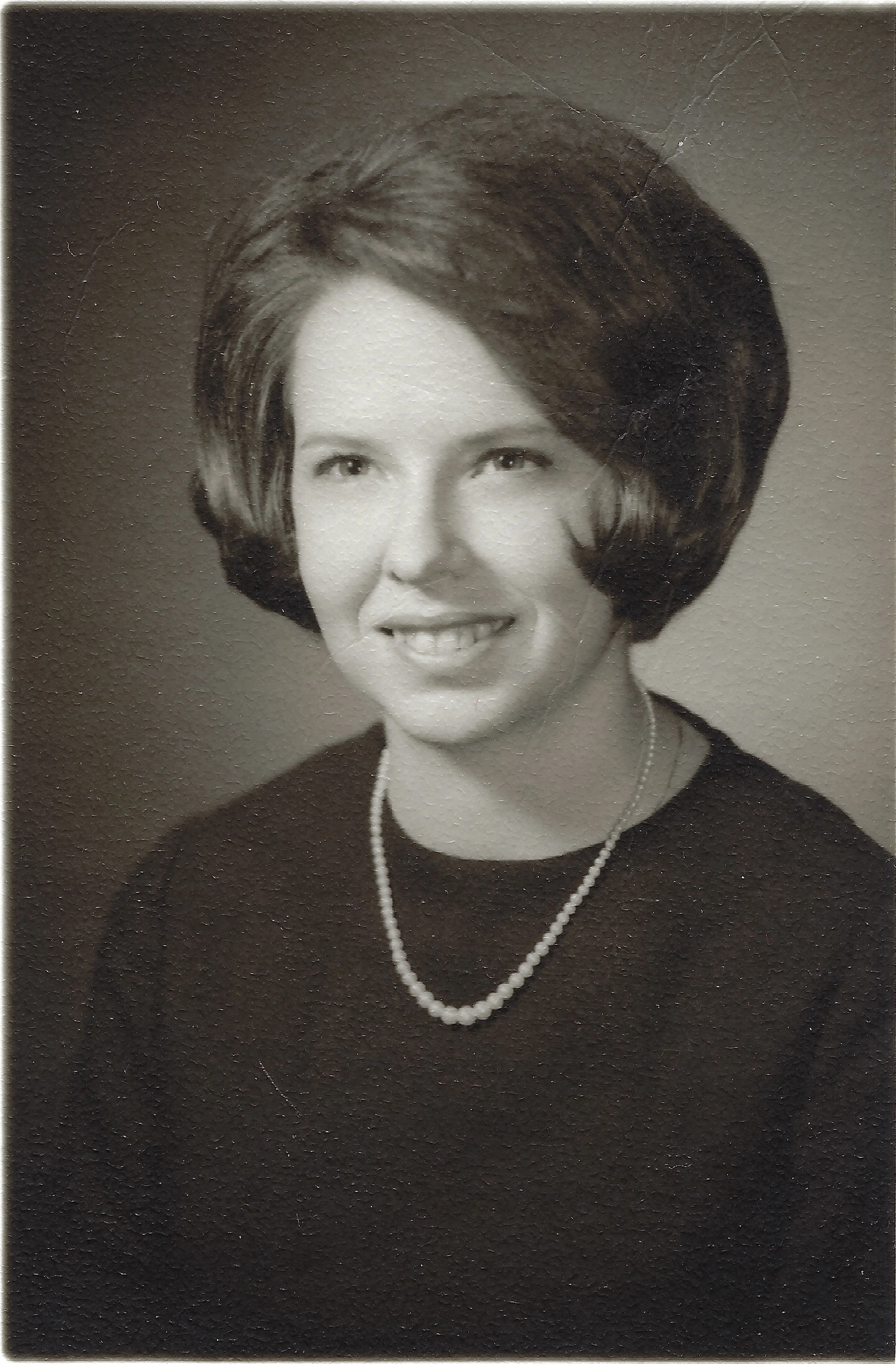 A black-and-white formal portrait of Cacky as a young woman in a pearl necklace and dark top, around 1966