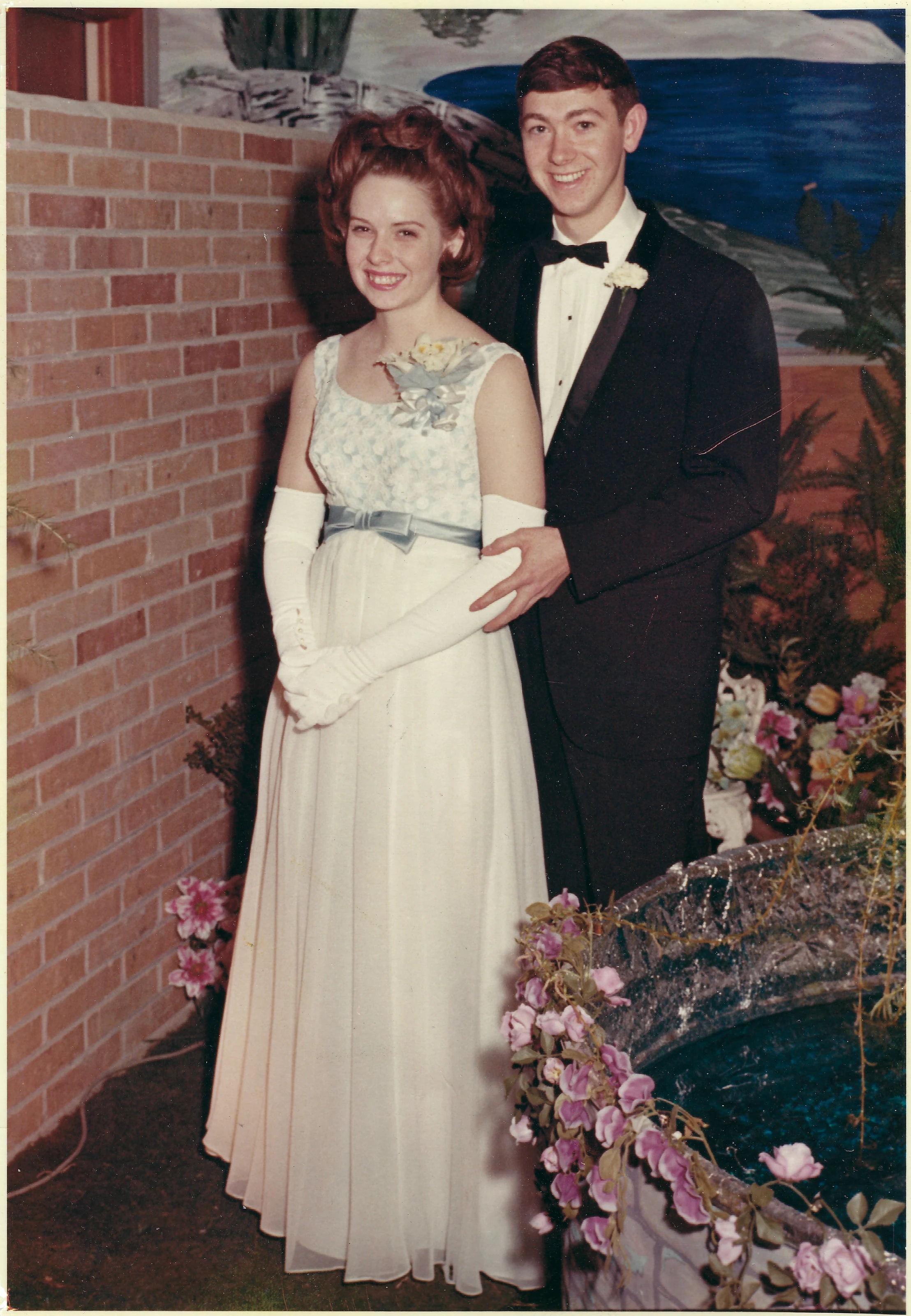 Cacky in a long formal gown and gloves beside a young man in a tuxedo at a college dance, around 1966
