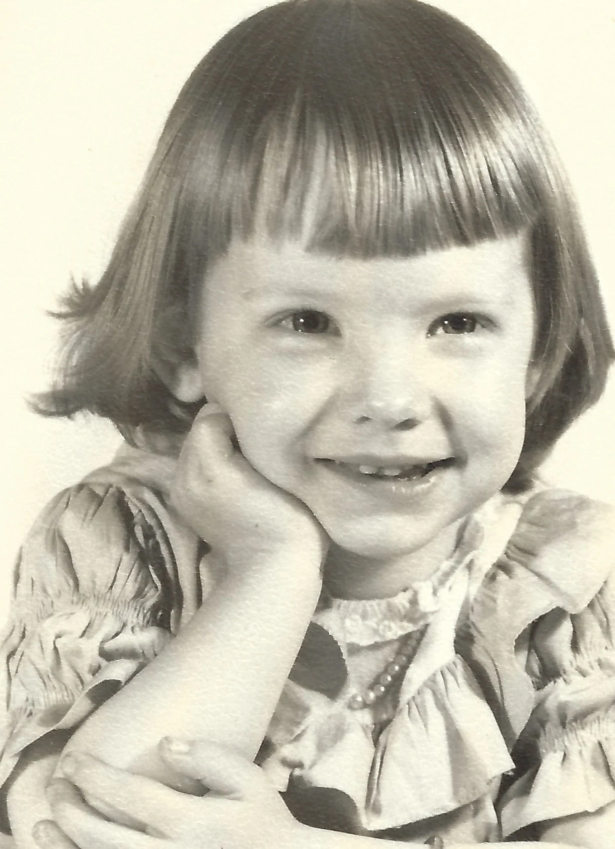 A studio portrait of Cacky as a young girl with a short bob and bangs, resting her chin on her hand, in a polka-dot dress, around 1951