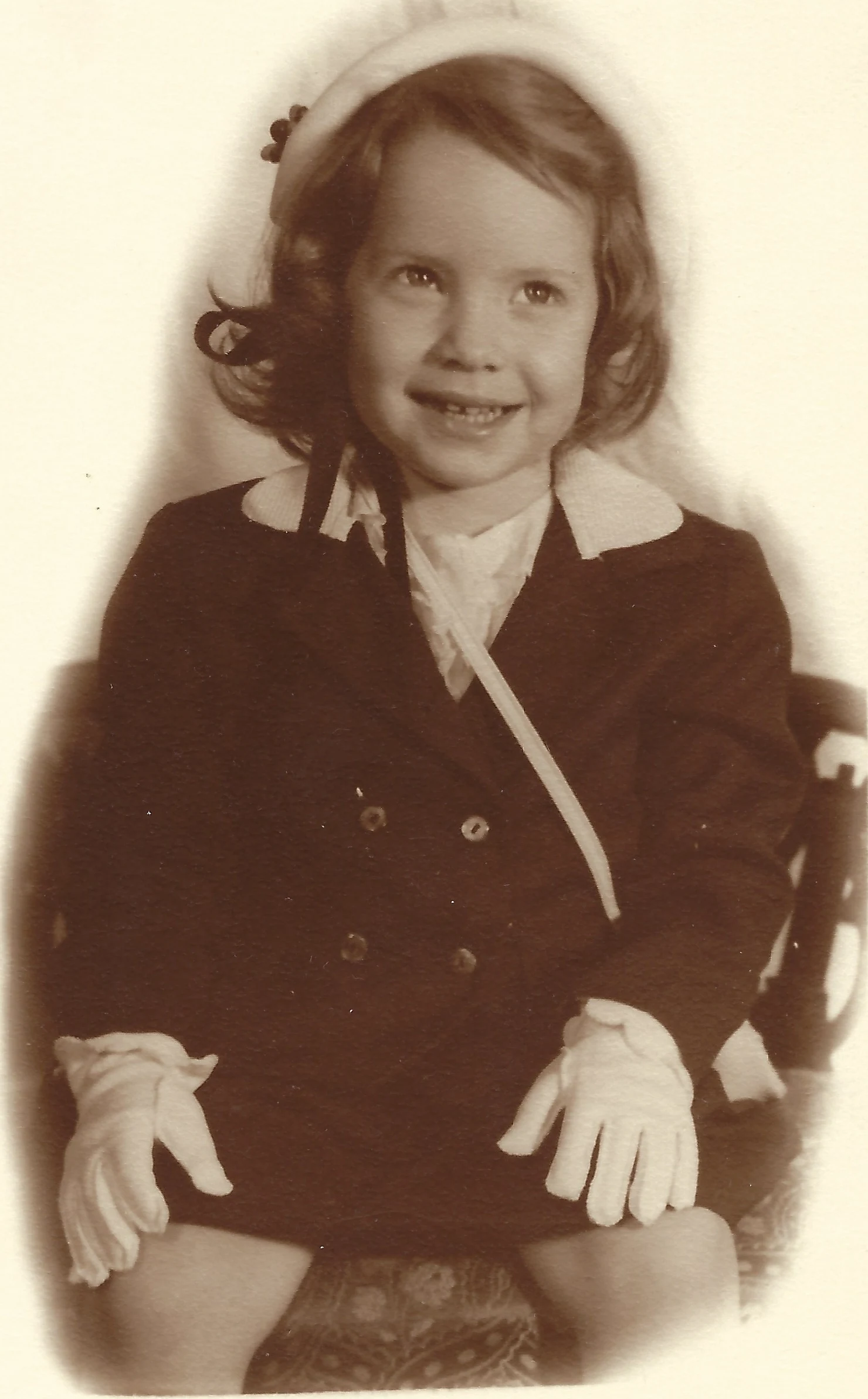 A sepia studio portrait of Cacky in a dark double-breasted coat, white beret, and white gloves, around 1953