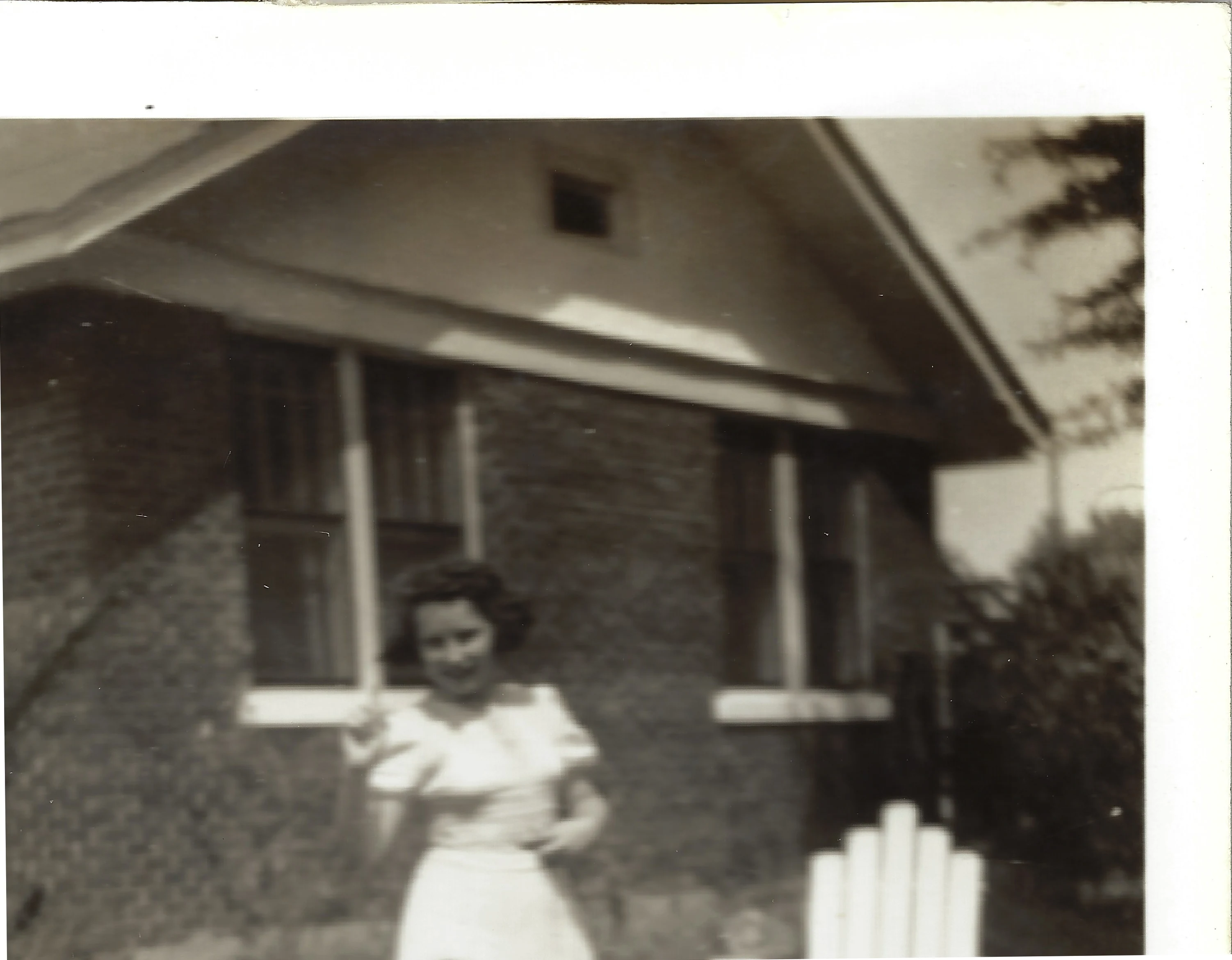 Gruzel (b.1924) as a young woman in a white blouse and skirt standing by a brick house, around 1943