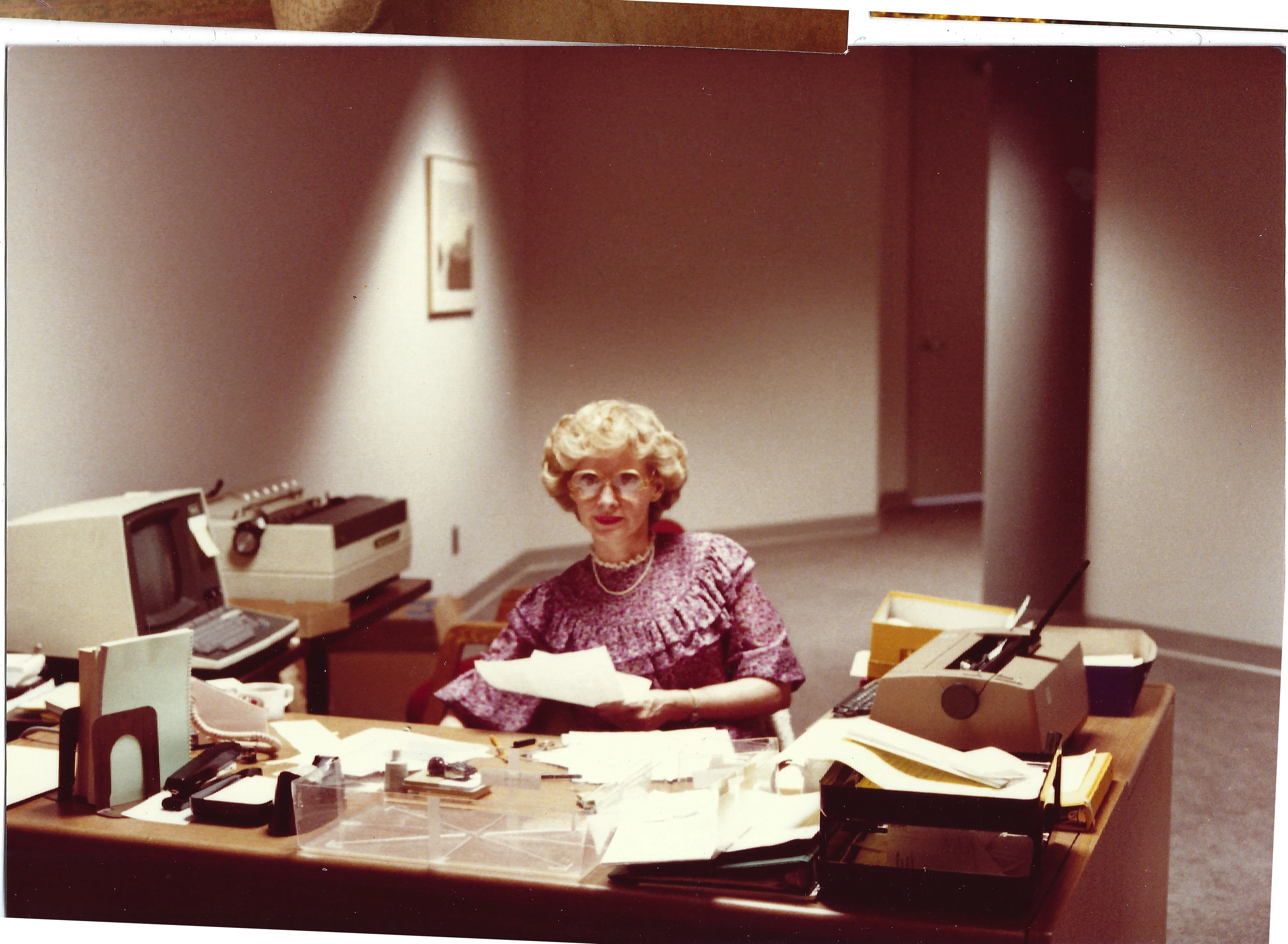 Gruzel (b.1924) seated at an office desk with papers, eyeglasses, and a typewriter, around 1994