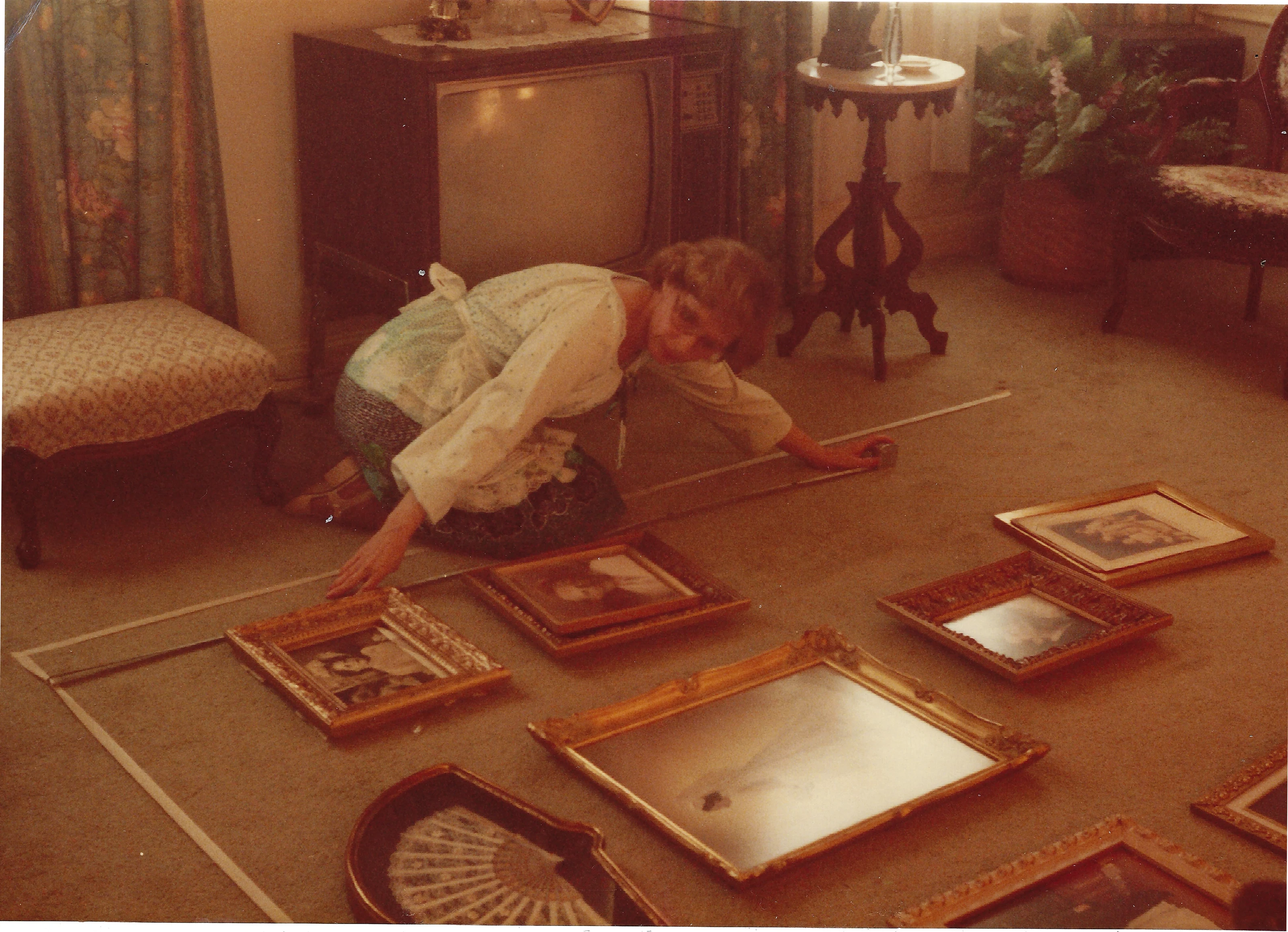 Gruzel (b.1924) with a tape measure arranging framed family portraits laid out on the carpet, around 1994