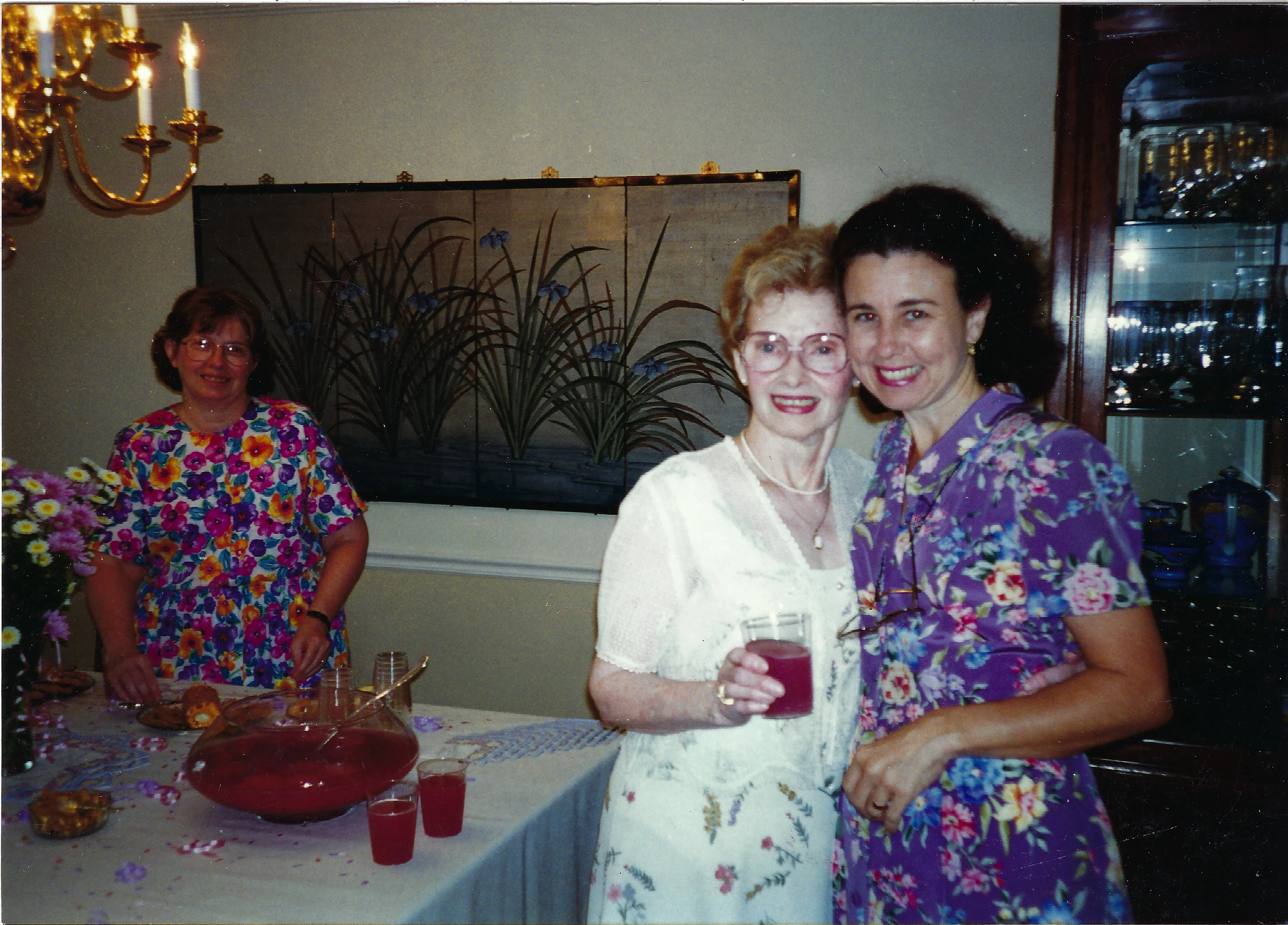 Gruzel (b.1924) in white lace embracing a guest at a gathering with a punch bowl; her daughter Cacky stands at the table in the background, around 1994