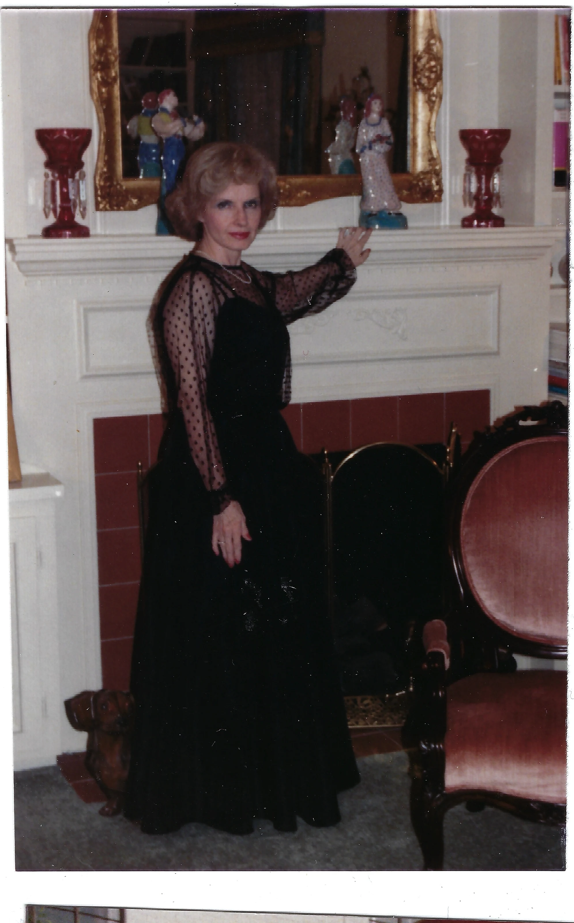 Gruzel (b.1924) in a black lace evening gown standing by a fireplace, around 1990