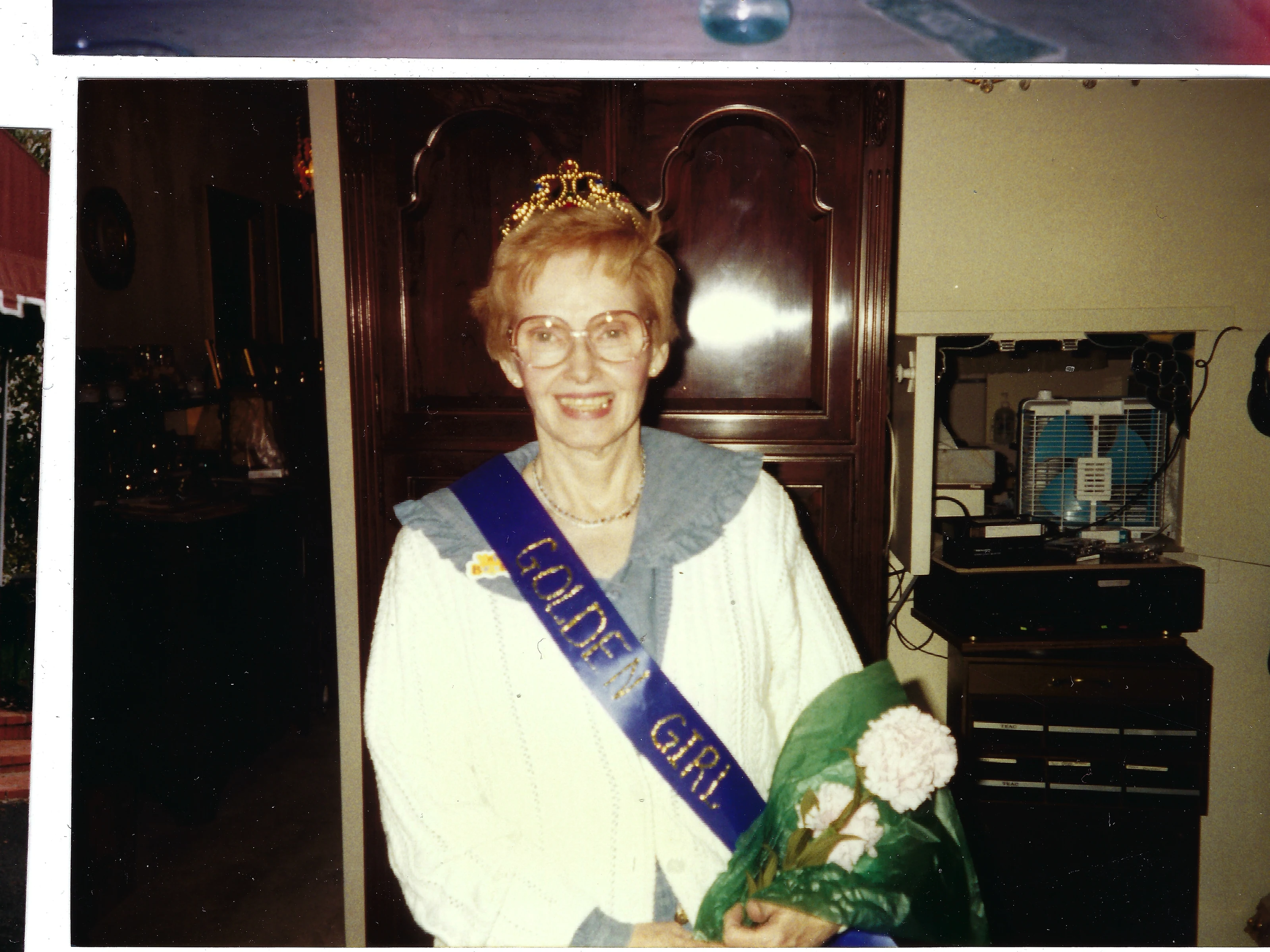 Gruzel (b.1924) wearing a 'Golden Girl' sash and tiara and holding flowers, around 1990
