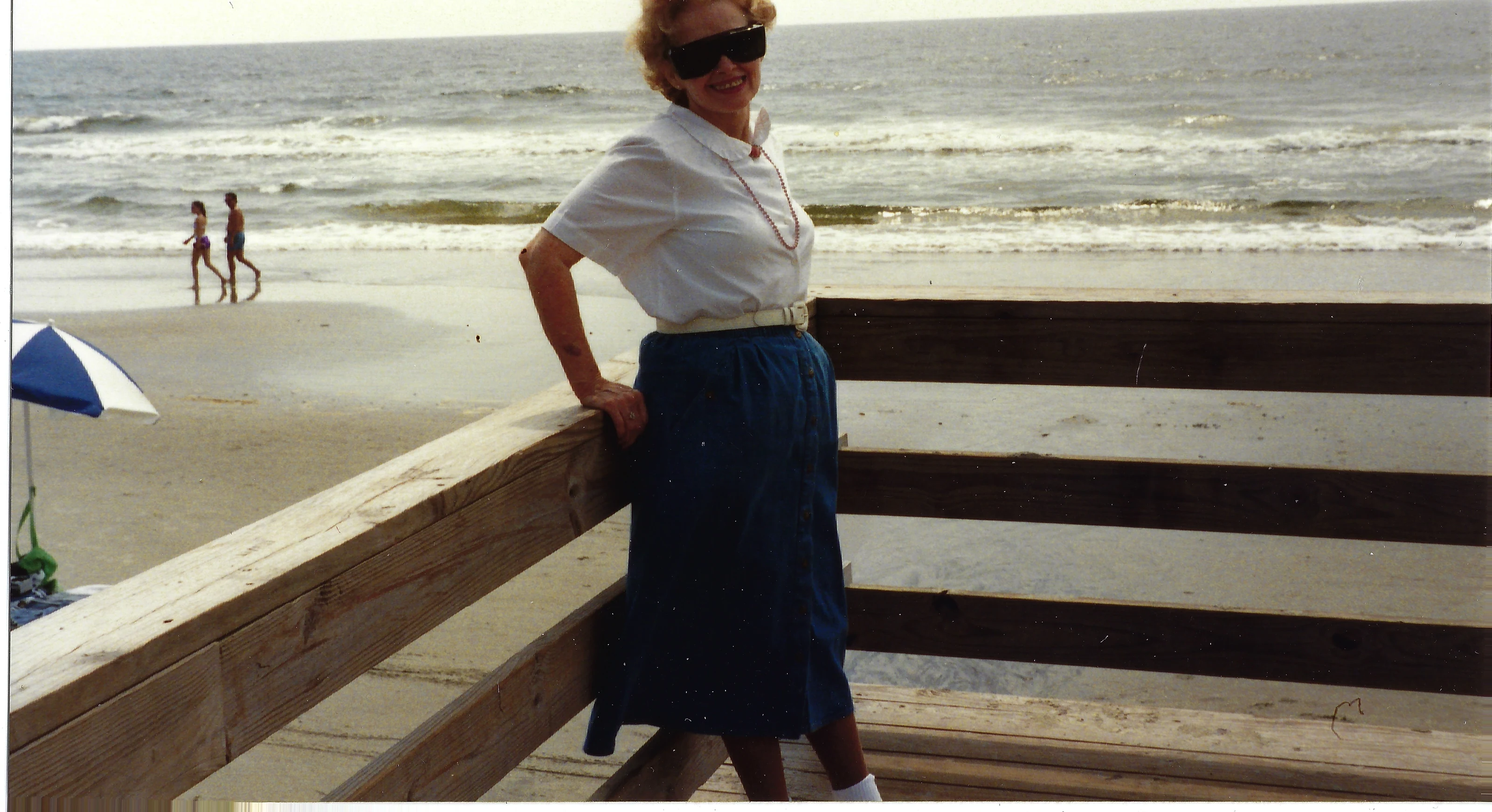 Gruzel (b.1924) in sunglasses leaning on a beach boardwalk railing, around 1990