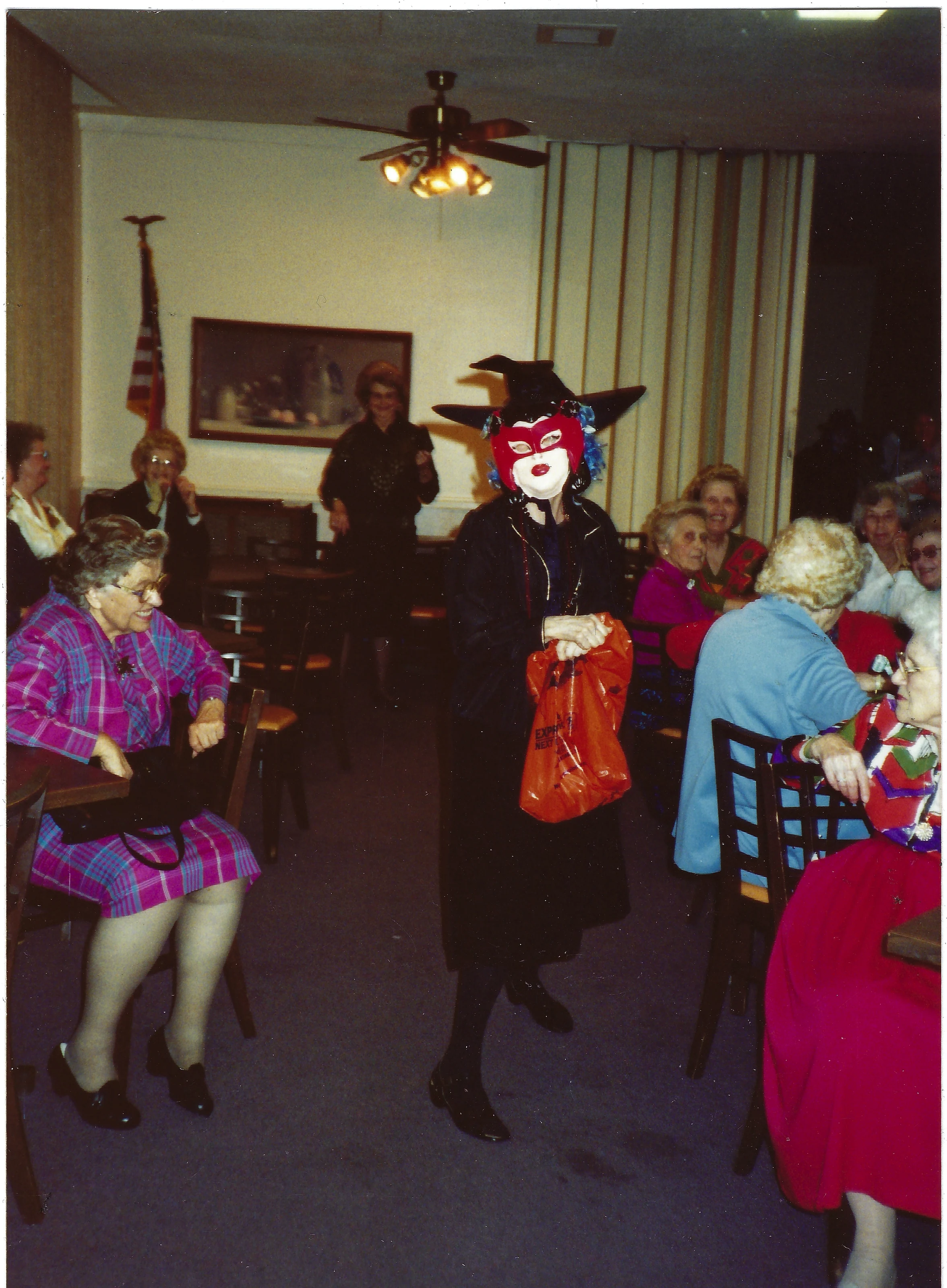 Another view of the costume party — Gruzel (b.1924) in her witch hat and mask, guests seated around the room, around 1993