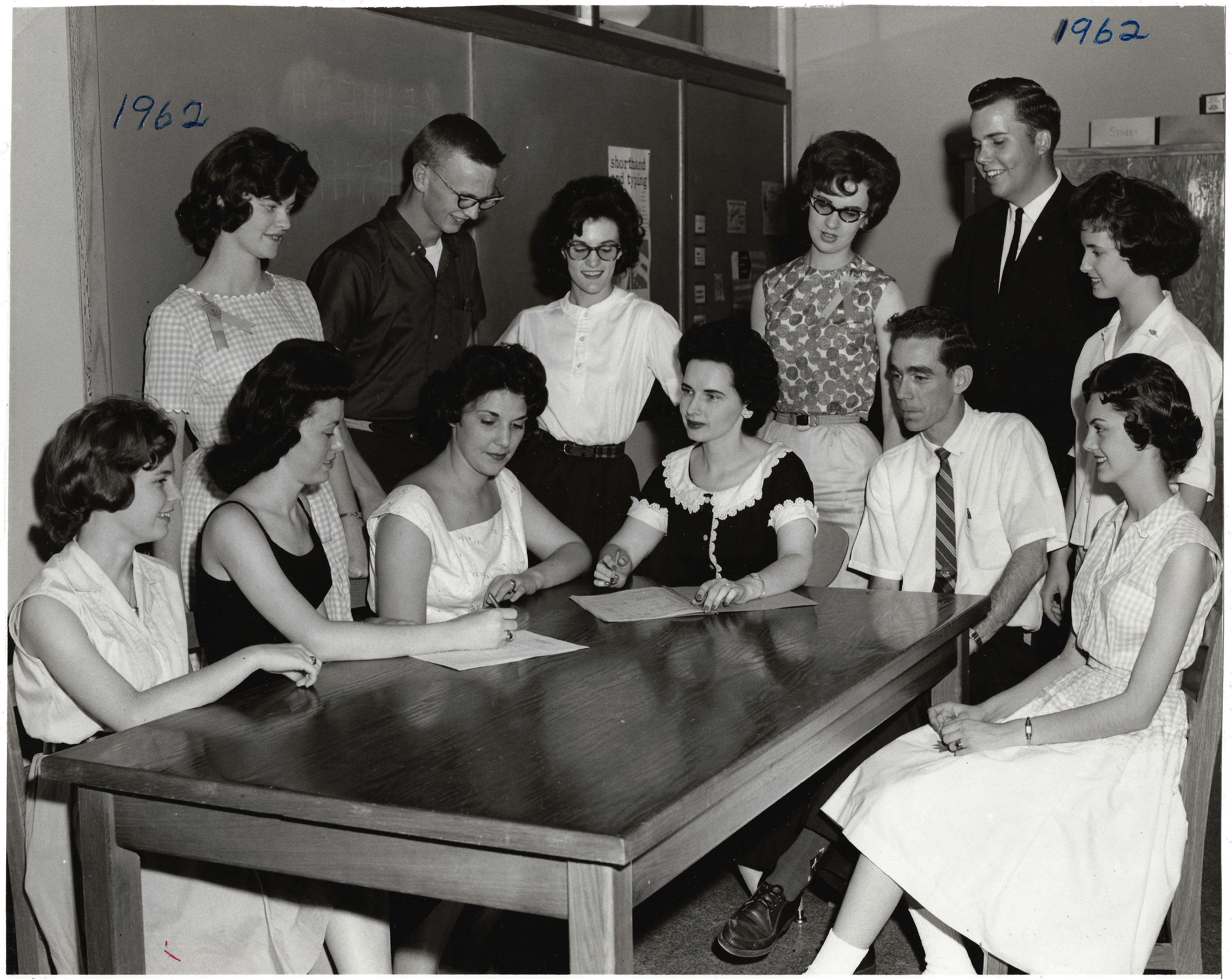 A 1962 group photograph of young people around a table with Mrs. Wilkins (Gruzel) and another instructor; the year is written on the photo