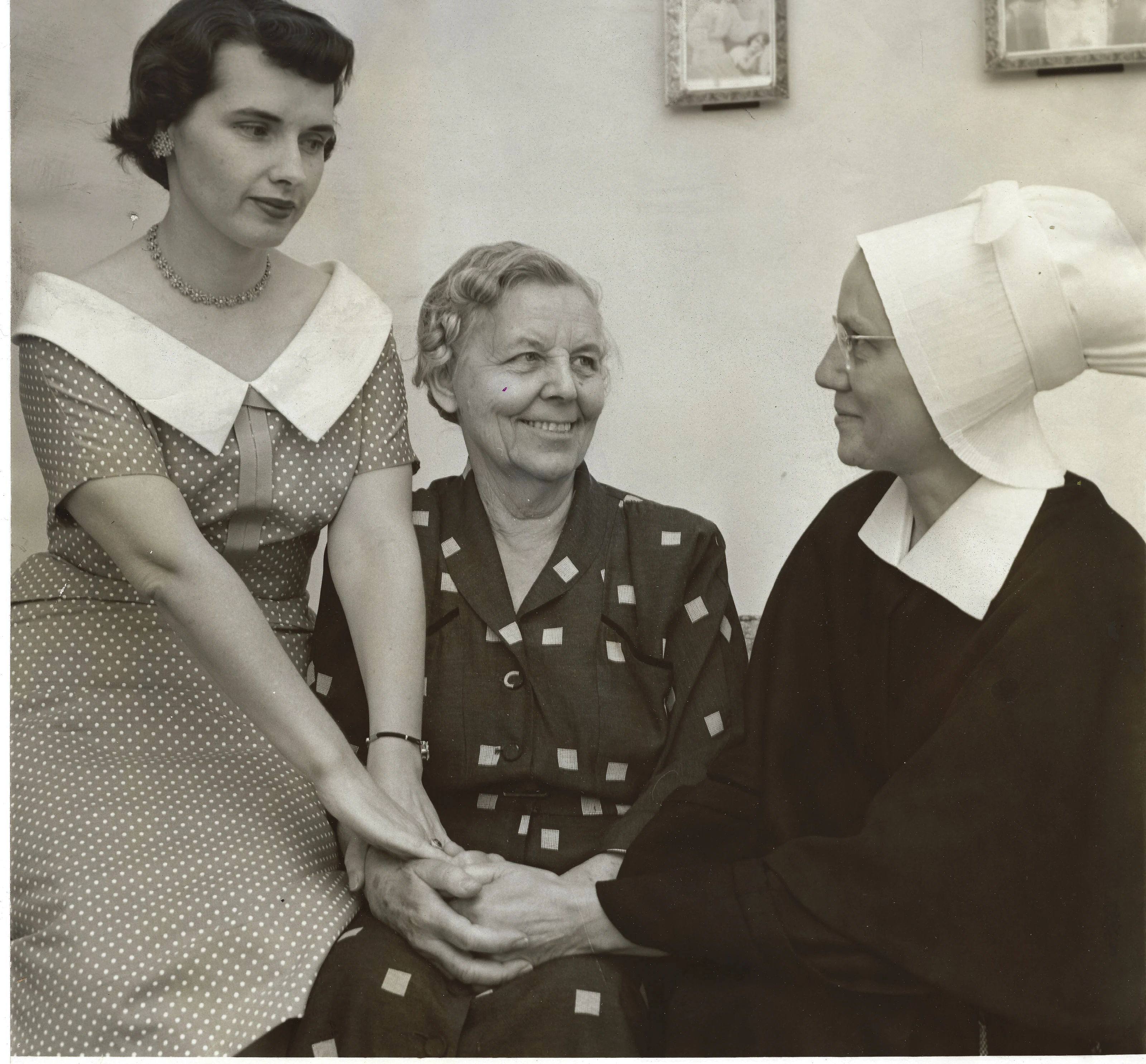 Gruzel (b.1924) in a polka-dot dress clasping hands with a smiling elderly woman seated and a woman in a nun's habit, around 1954