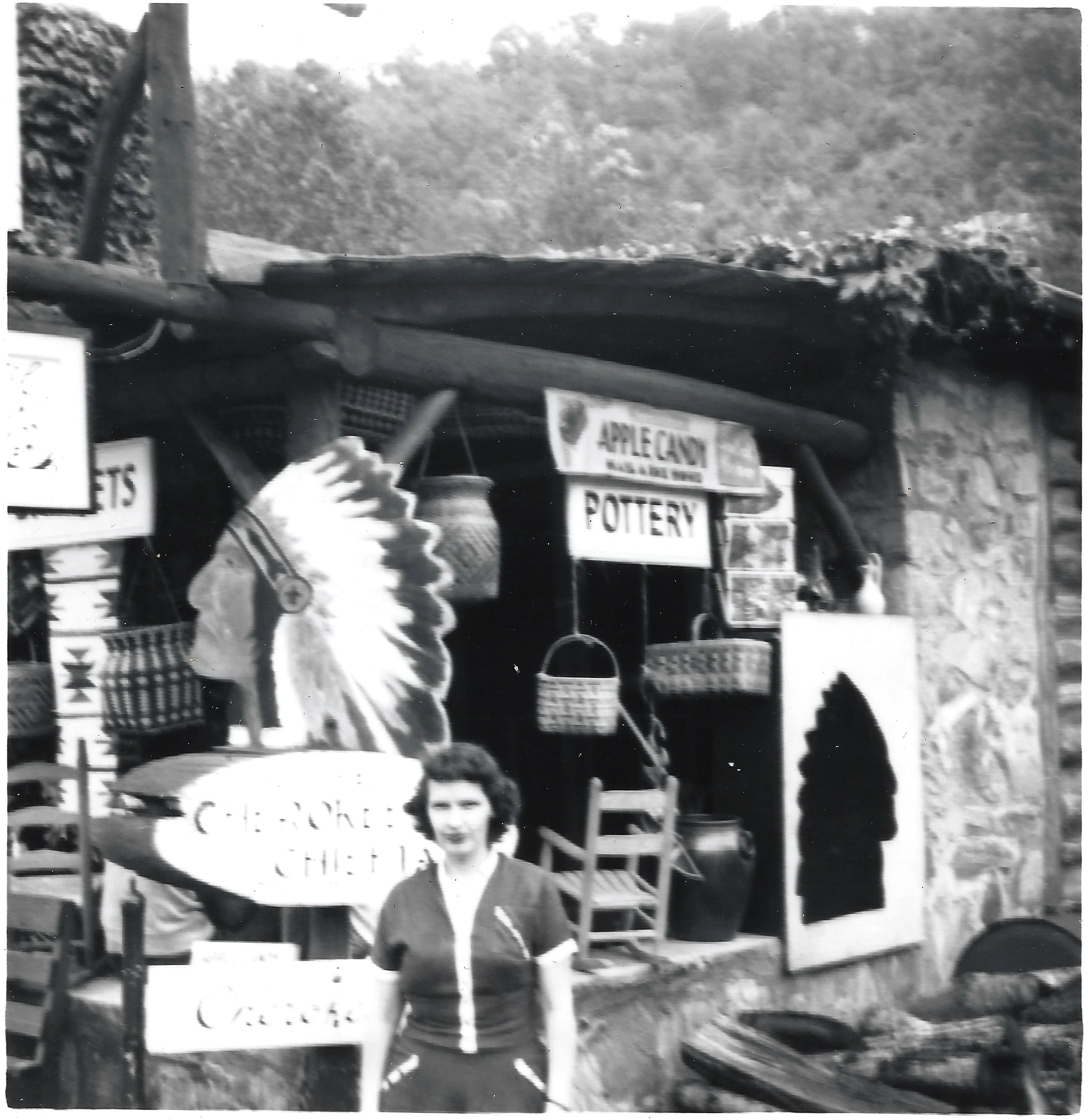 Gruzel (b.1924) standing before a roadside trading post hung with baskets and signs for pottery and apple candy, around 1954
