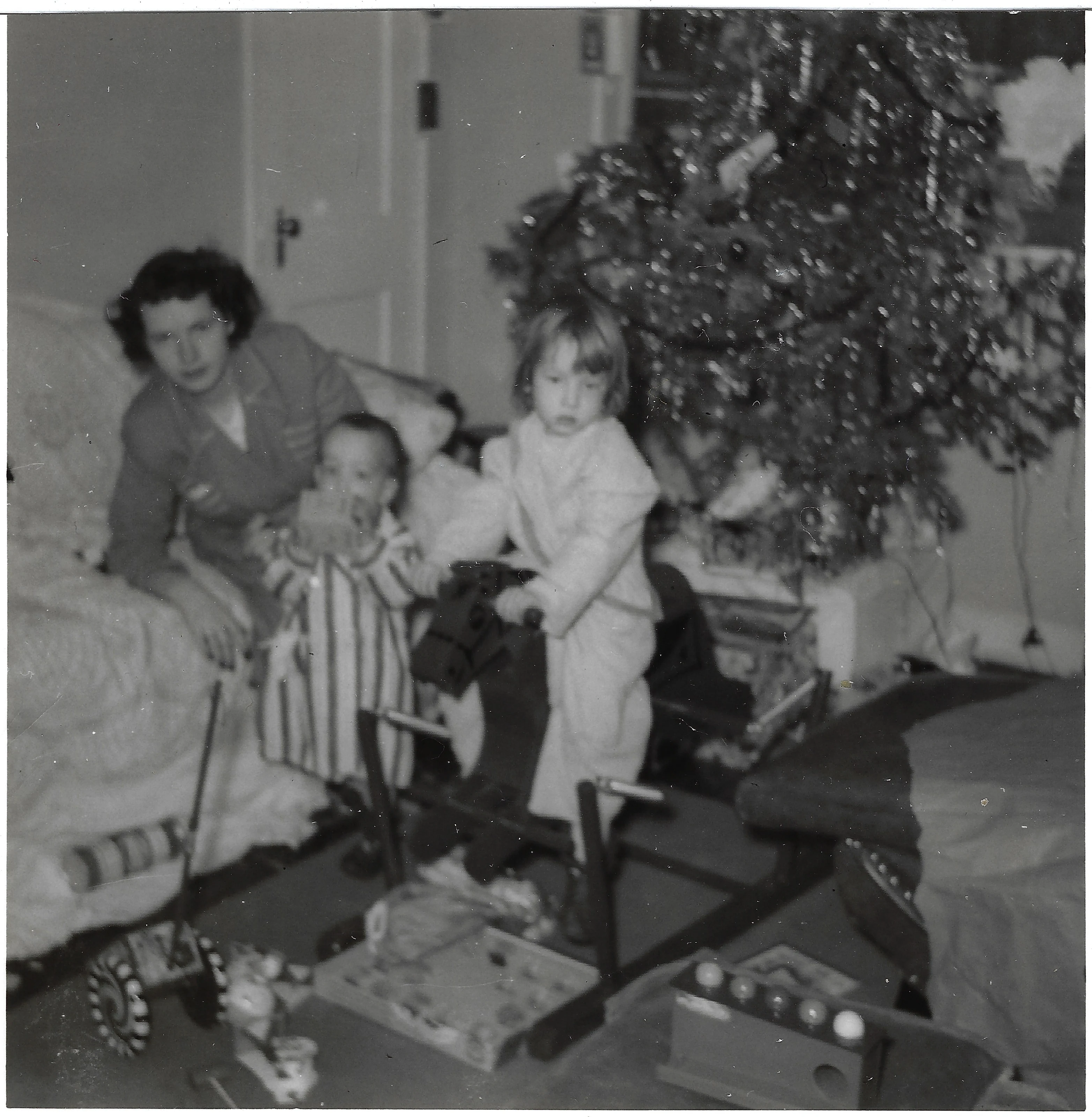 Gruzel (b.1924) by the bed on Christmas morning with her two small children — David Earle in striped pajamas and Cacky on a rocking horse — beside the decorated tree, around 1951