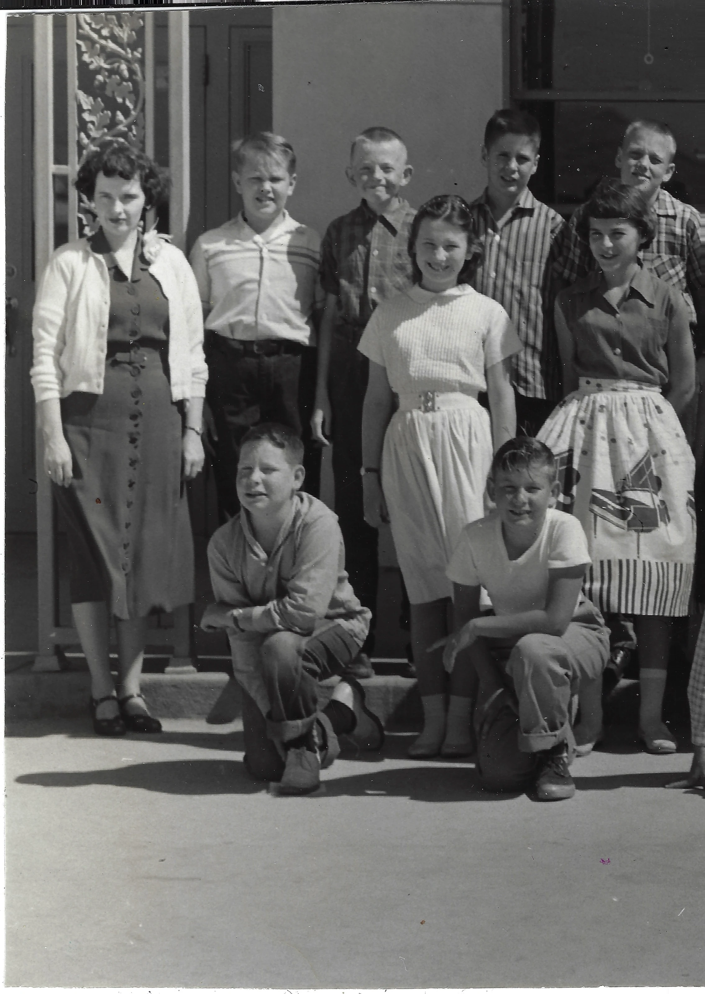 Gruzel (b.1924) in a cardigan standing with a group of school-age children on steps, around 1962
