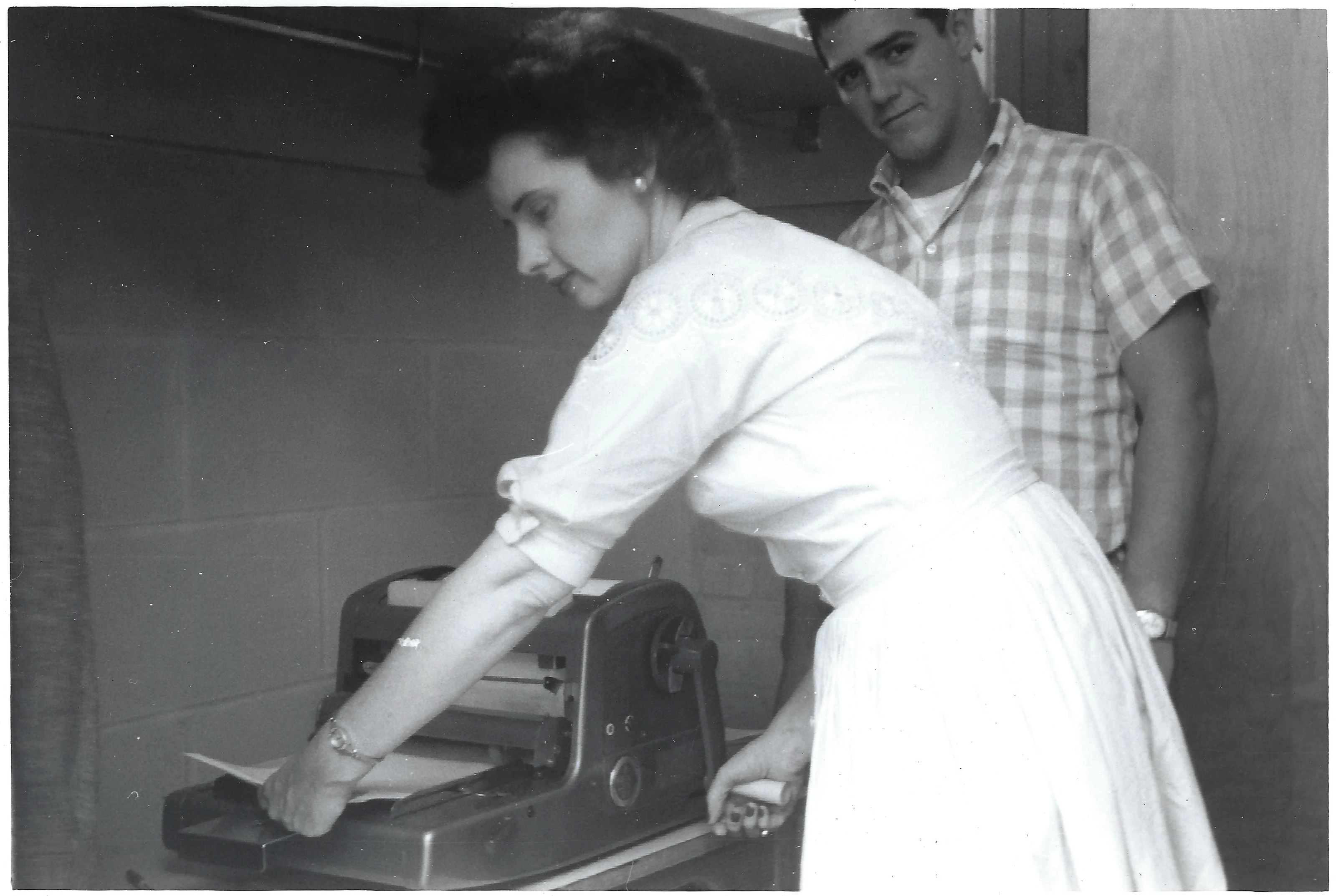 Gruzel (b.1924) feeding paper into a mimeograph machine while a young man looks on, around 1962