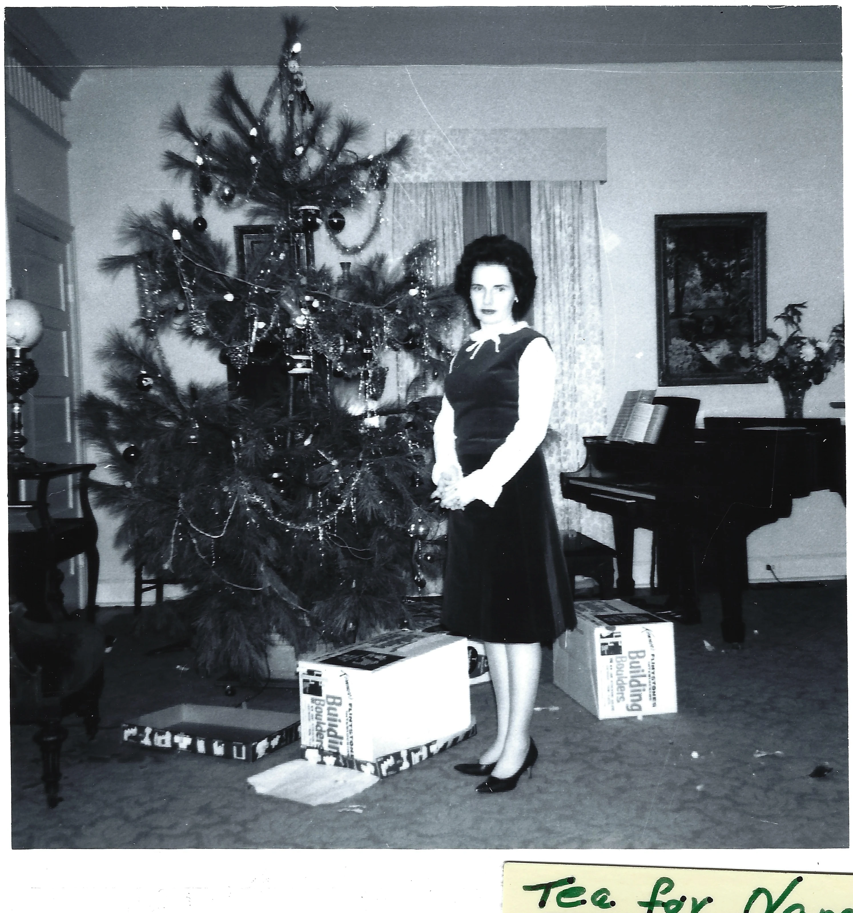 Gruzel (b.1924) in a dark dress standing by a decorated Christmas tree near a grand piano in January 1967
