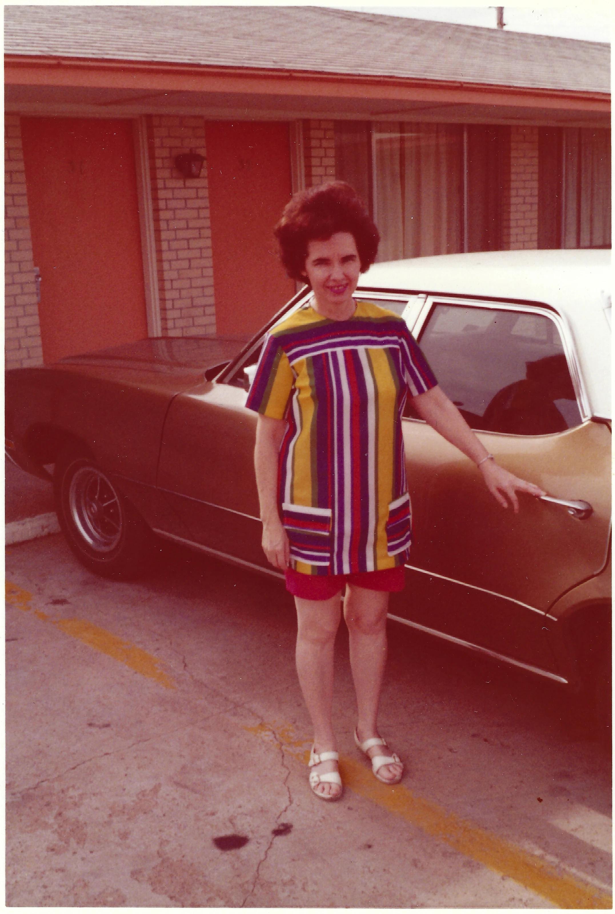 Gruzel (b.1924) in a striped mini-dress standing by a car at a motel, around 1971