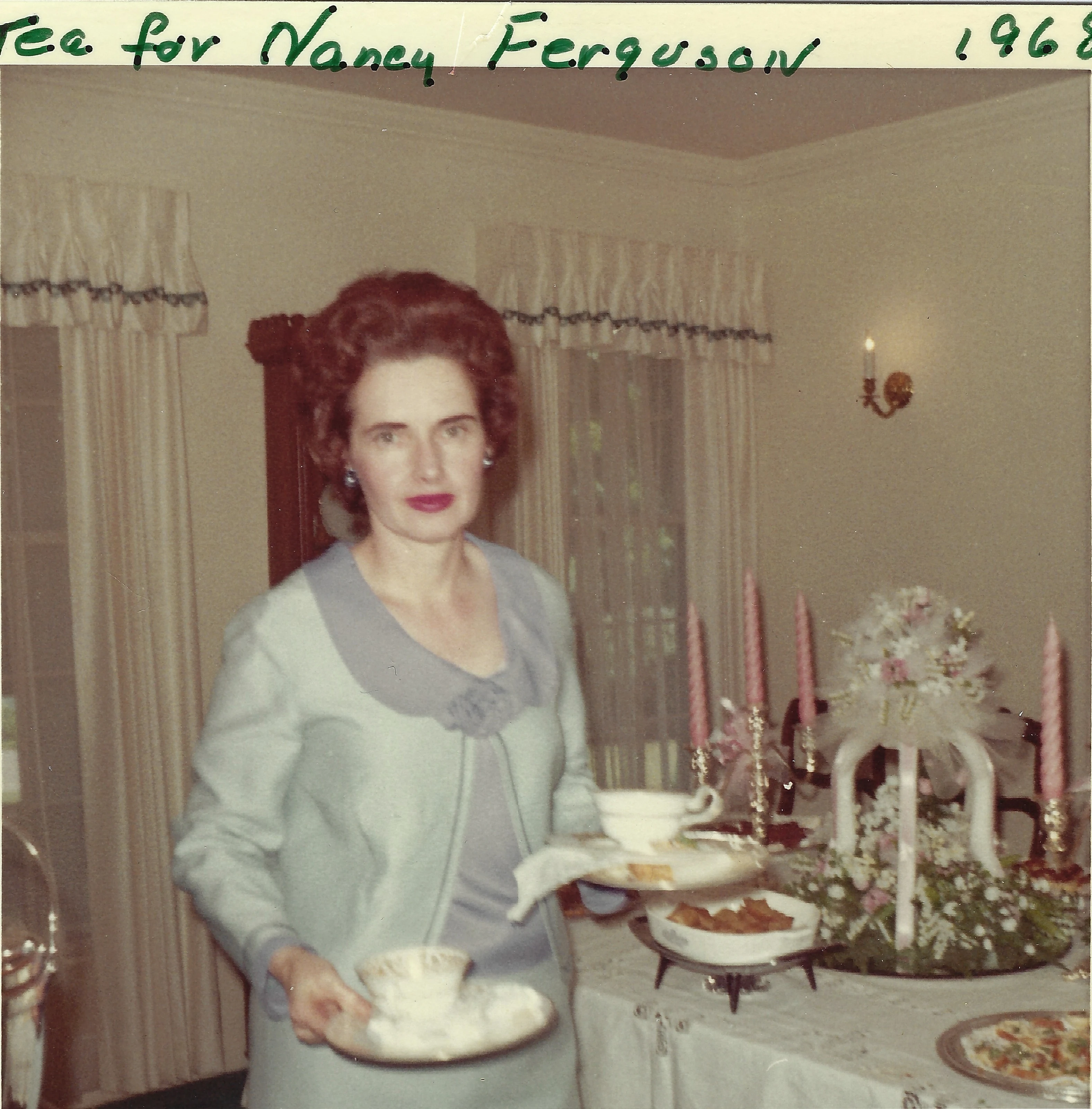 Gruzel (b.1924) in a blue dress holding teacups at a decorated tea table, the print captioned 'Tea for Nancy Ferguson 1968'