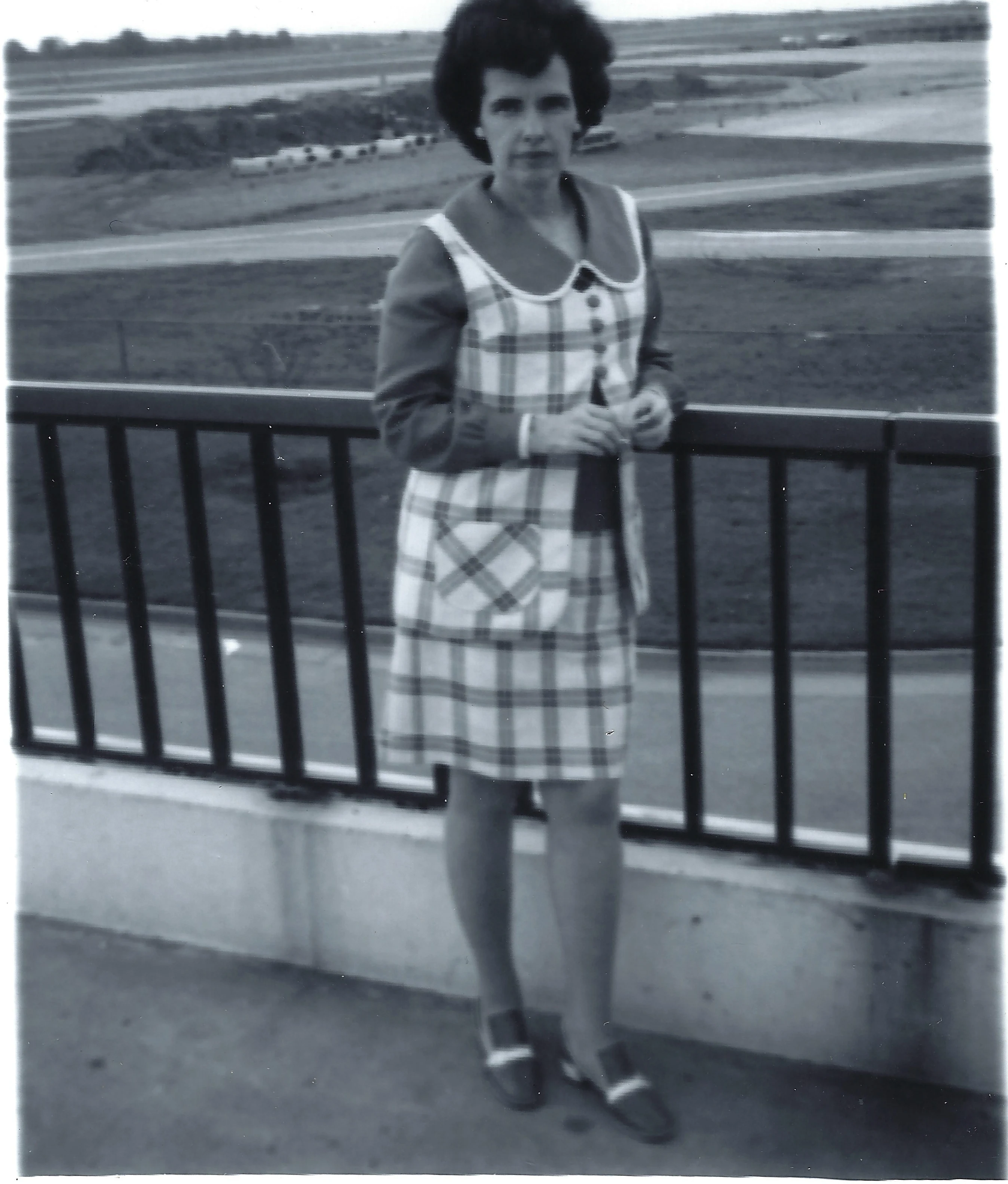 Gruzel (b.1924) in a plaid jumper standing at a railing overlooking a highway, around 1966