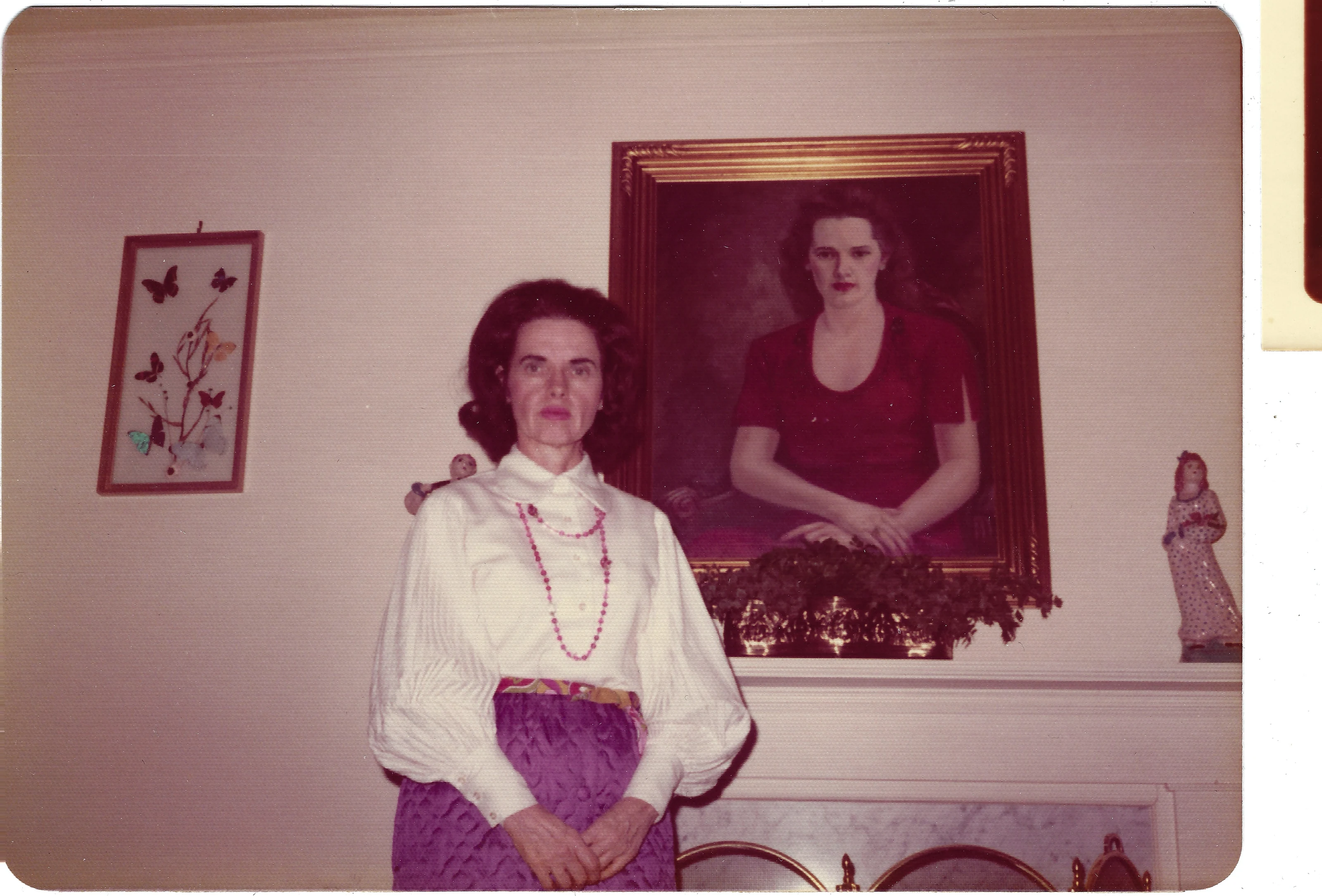 Gruzel (b.1924) standing beside a framed 1940s painted portrait of herself as a young woman, around 1973