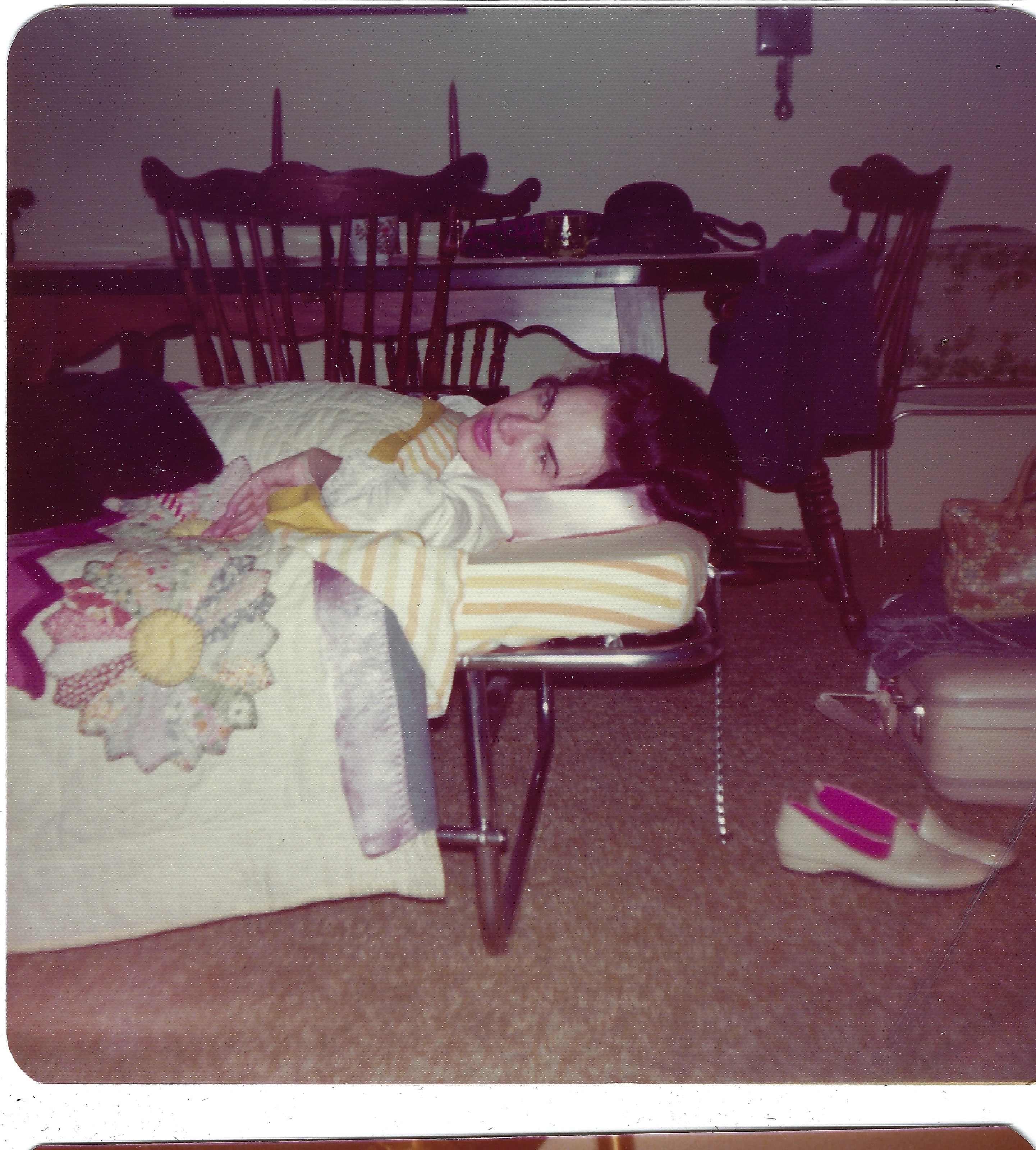 Gruzel (b.1924) resting on a chair with a neck pillow beside a dining table, around 1974