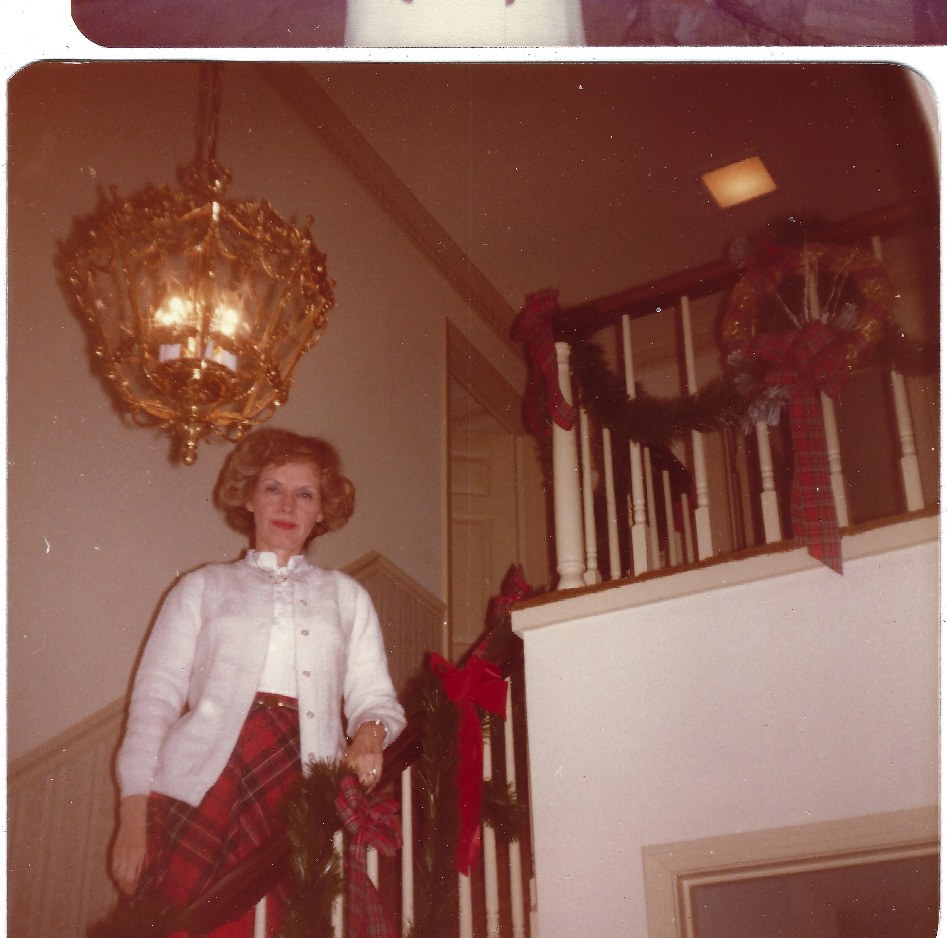 Gruzel (b.1924) in a white cardigan and plaid skirt on a garland-decorated staircase at Christmas, around 1981