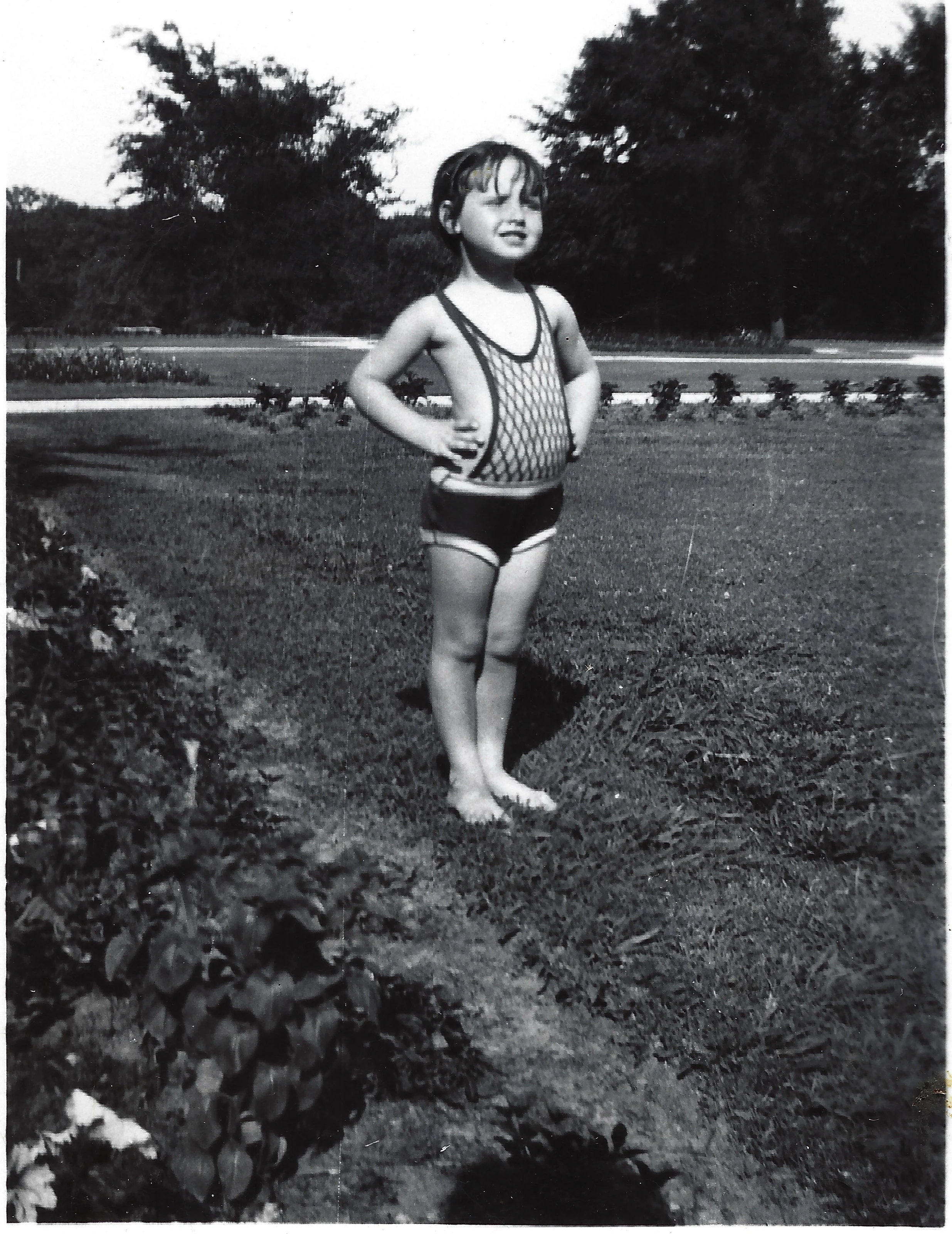 Gruzel (b.1924) as a young child in a 1920s-style knit swimsuit, standing with hands on hips on a park lawn, around 1930
