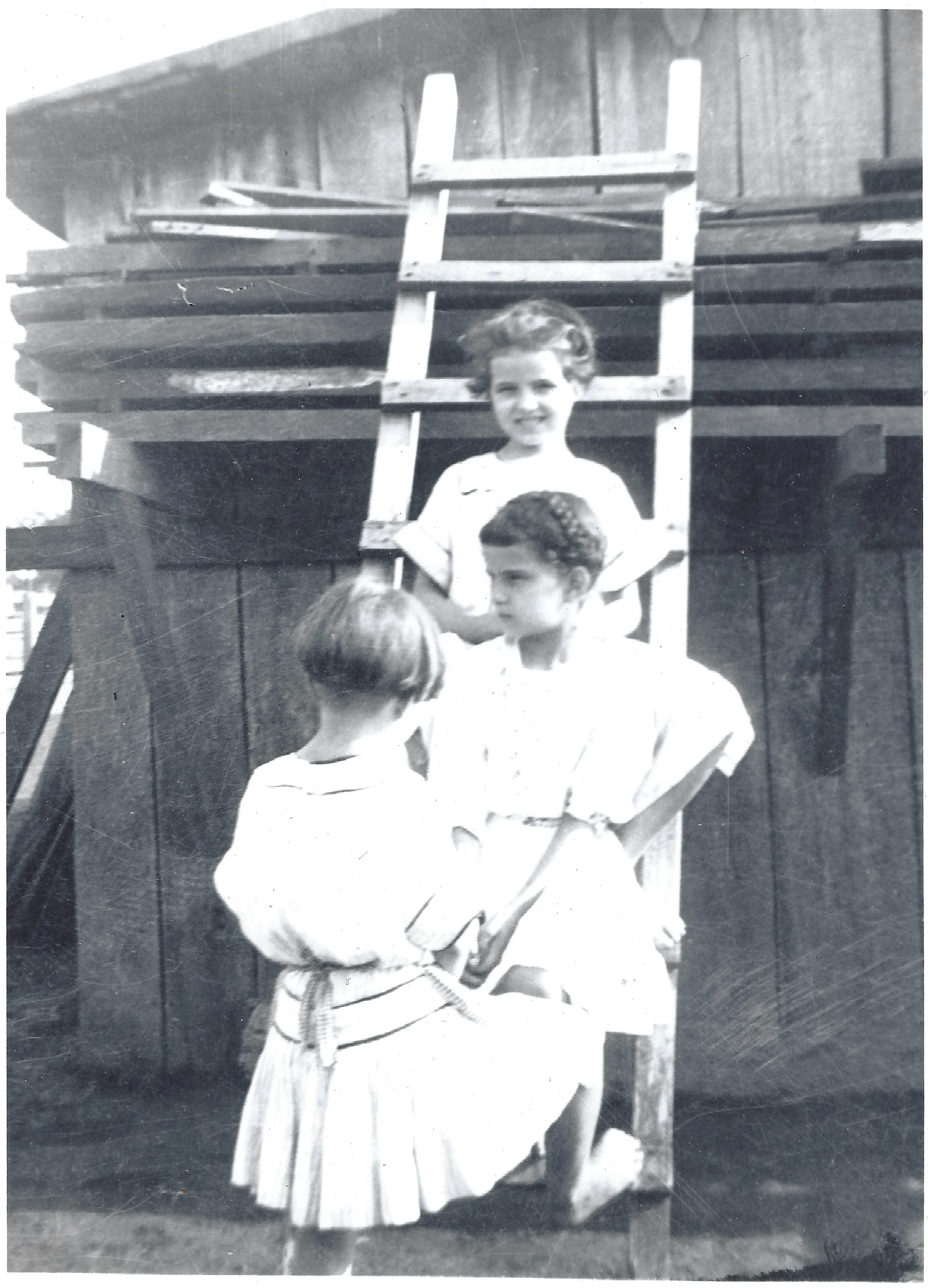 Three children beside a wooden shed with a leaning ladder, Mama Percy among them, May 1915