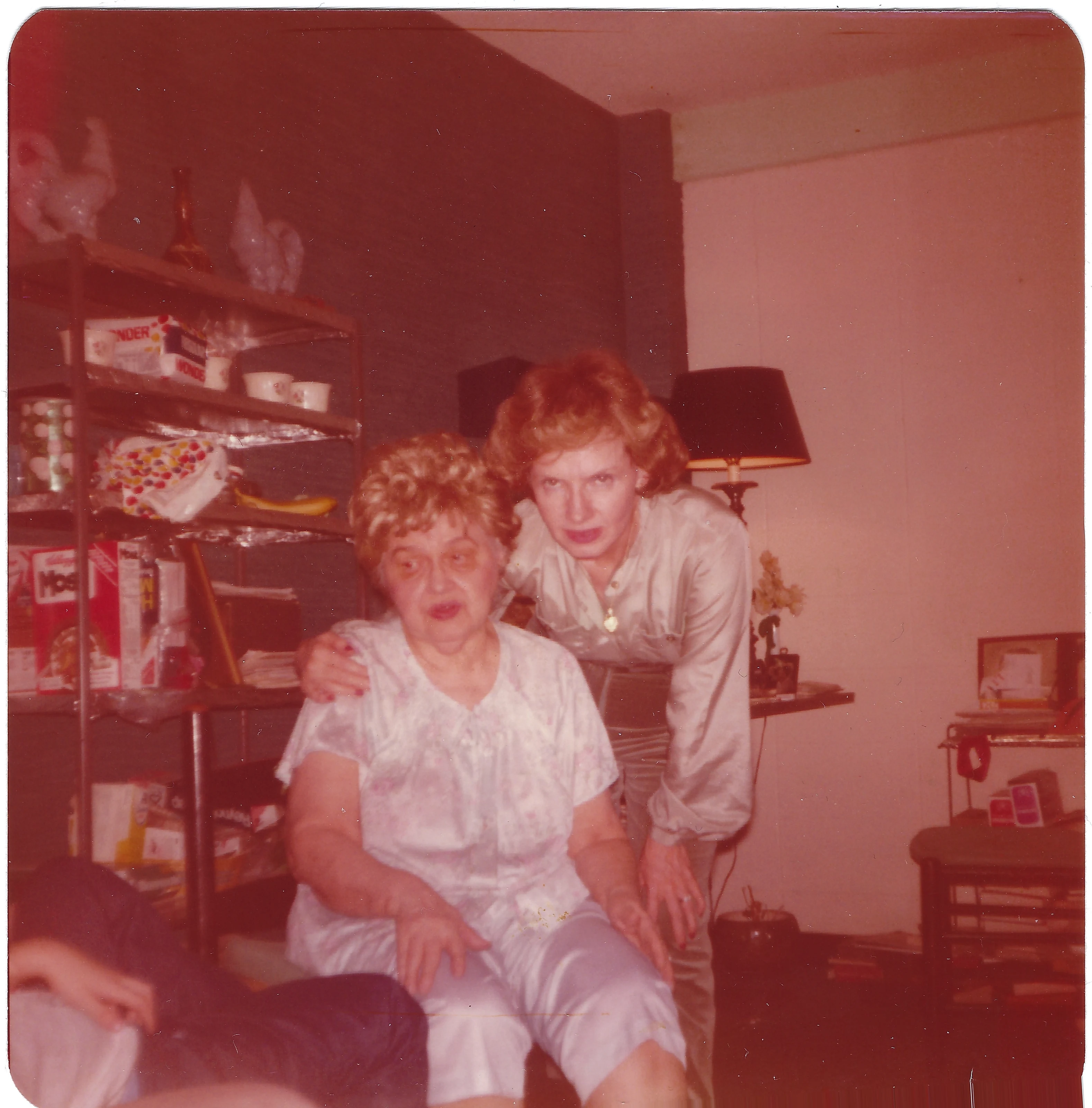 Gruzel leaning over Mama Percy (Catherine Fleming) seated in a room, around 1977