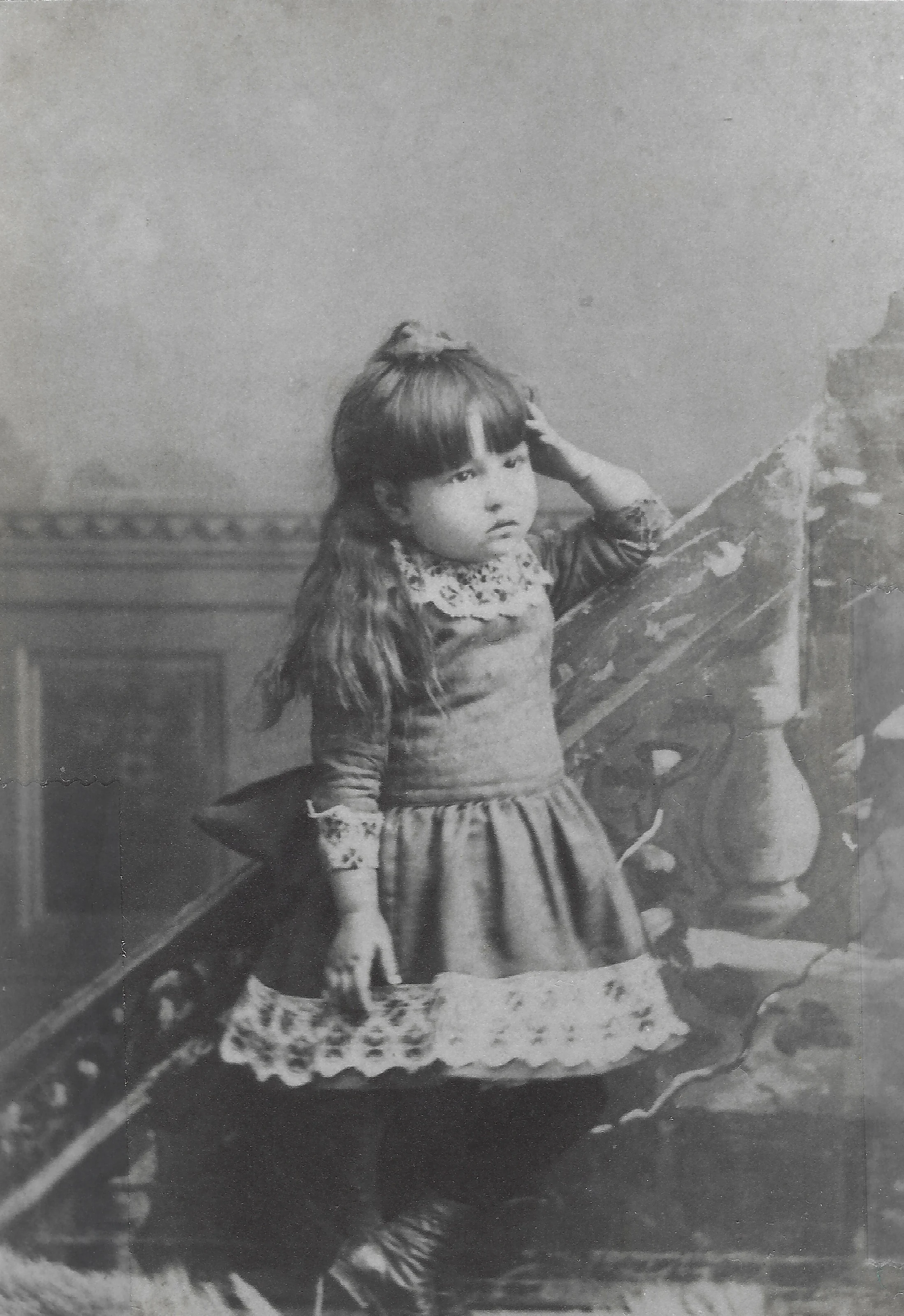 Mama Percy (Catherine Fleming) as a young girl leaning on the banister of an ornate staircase, around 1908