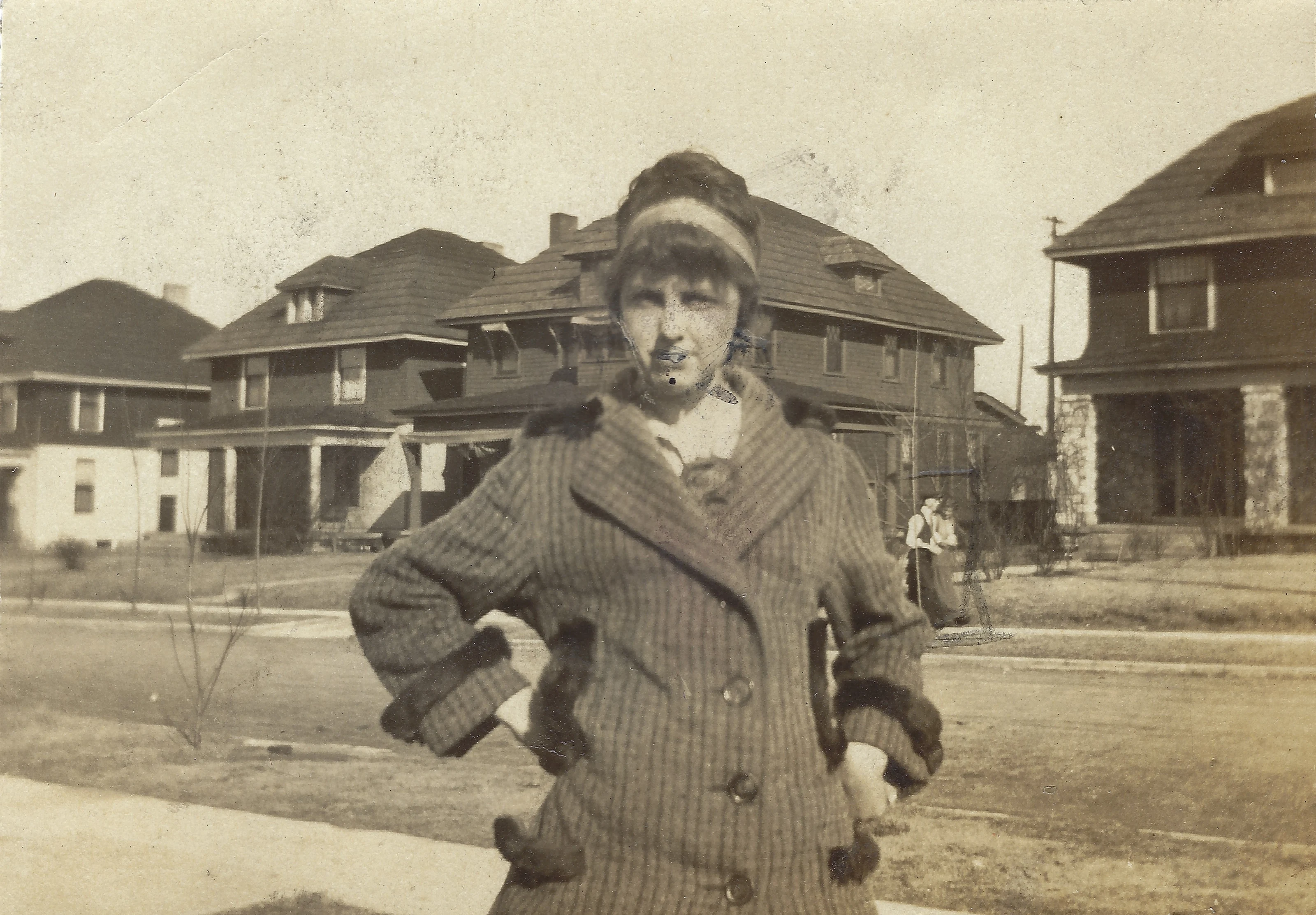 Mama Percy (Catherine Fleming) as a teenager in a fur-trimmed striped winter coat and hat on a residential street, around 1918