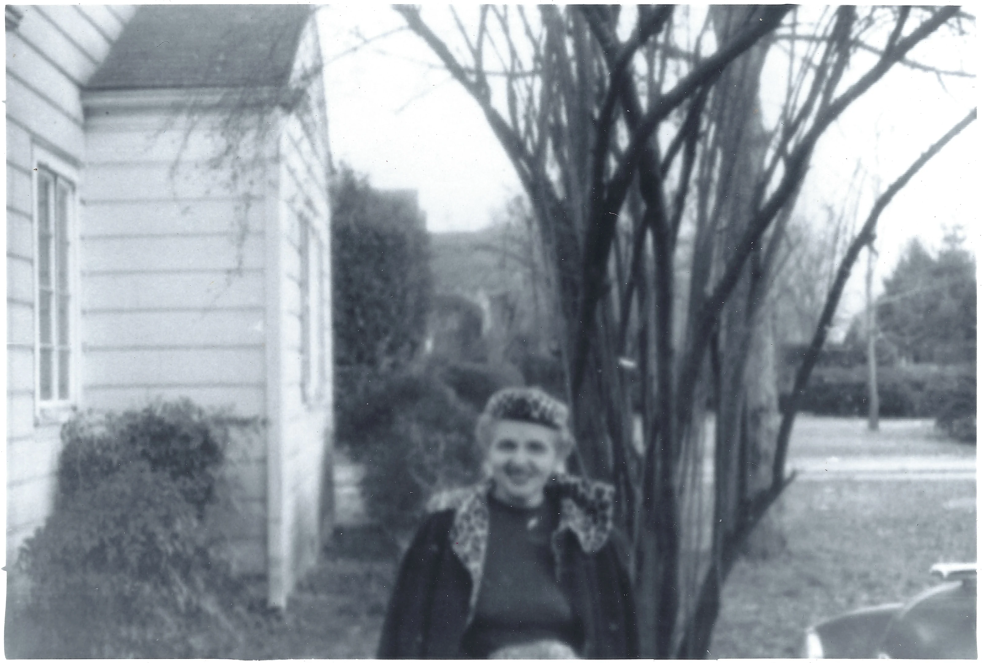 Mama Percy (Catherine Fleming) standing by a bare garden tree beside the house, February 1969