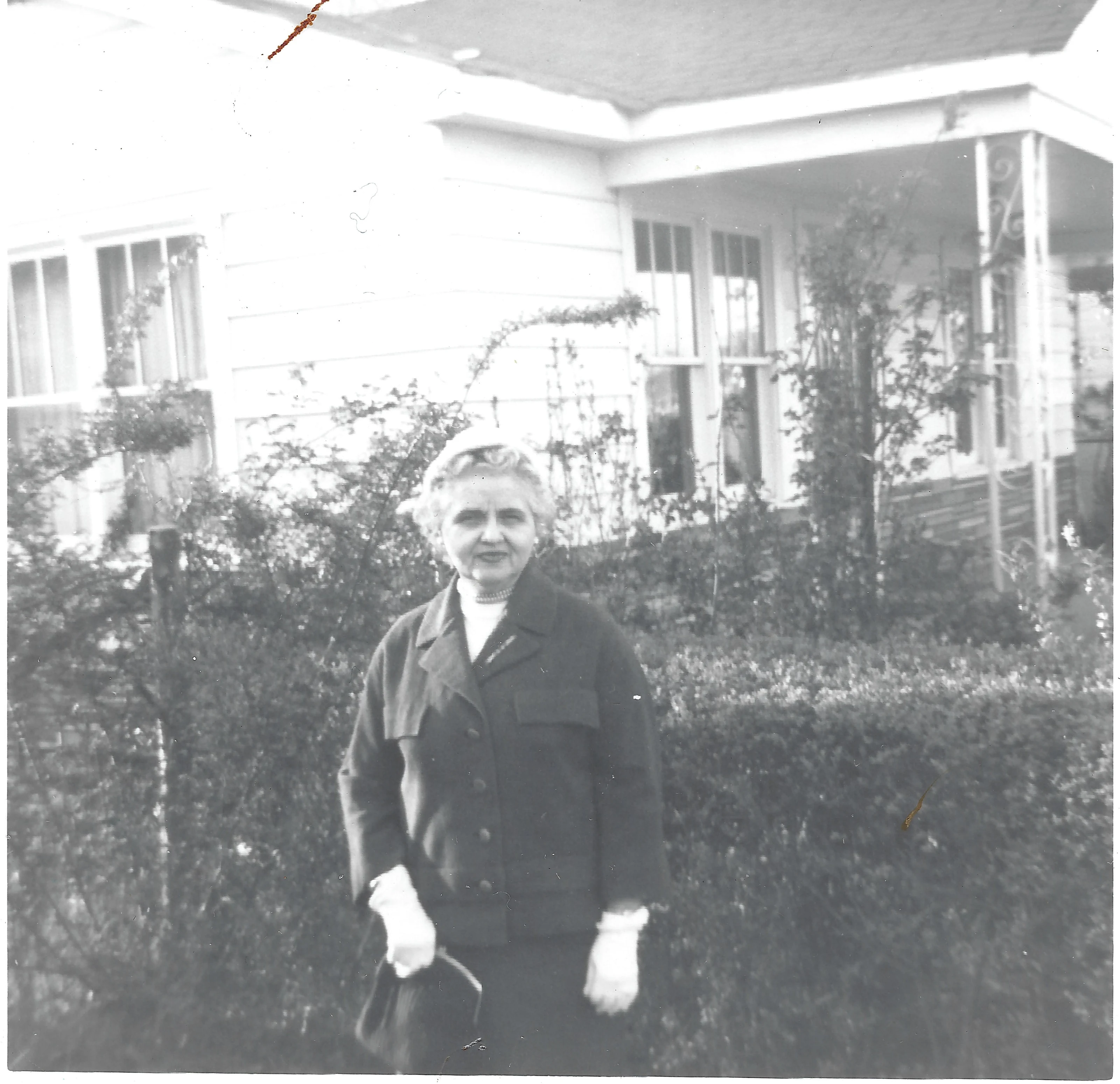 Mama Percy (Catherine Fleming) in a suit and gloves standing in front of a porch, around 1963
