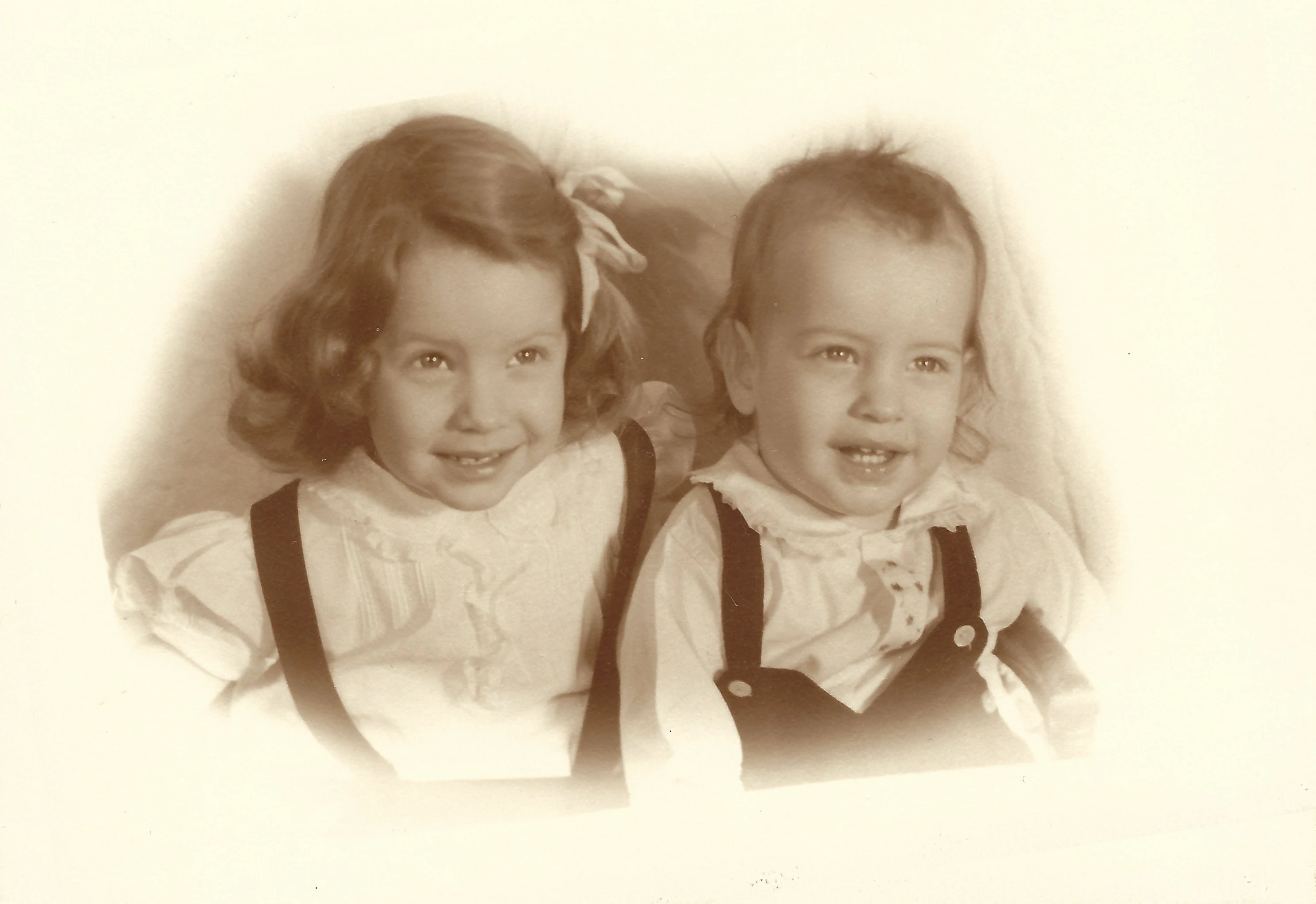 A sepia studio portrait of Cacky (b.1947) with a hair bow and her younger brother David Earle Wilkins in suspenders, around 1952