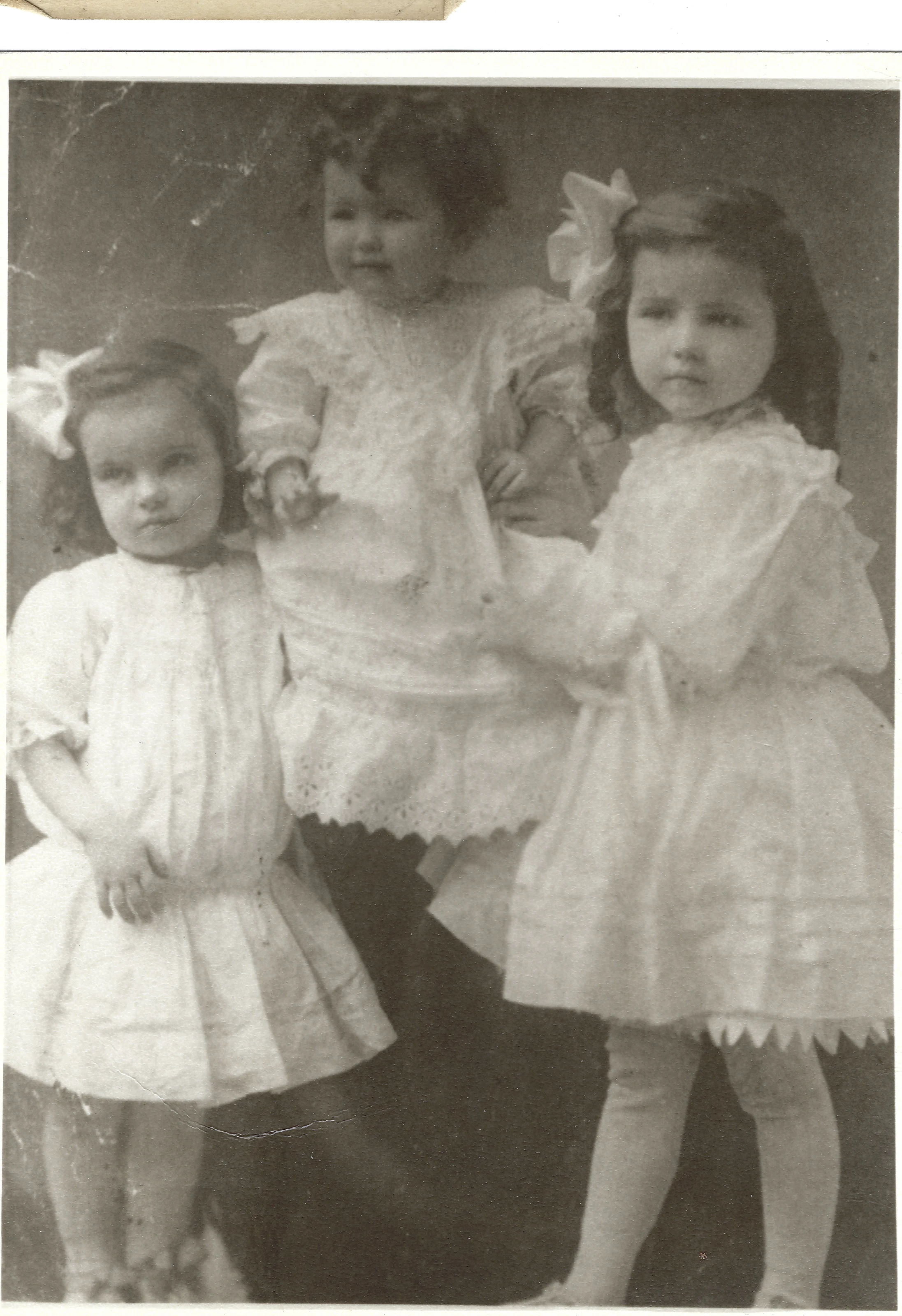 Studio portrait of three young girls in white dresses with a baby in lace, Mama Percy among them, around 1908